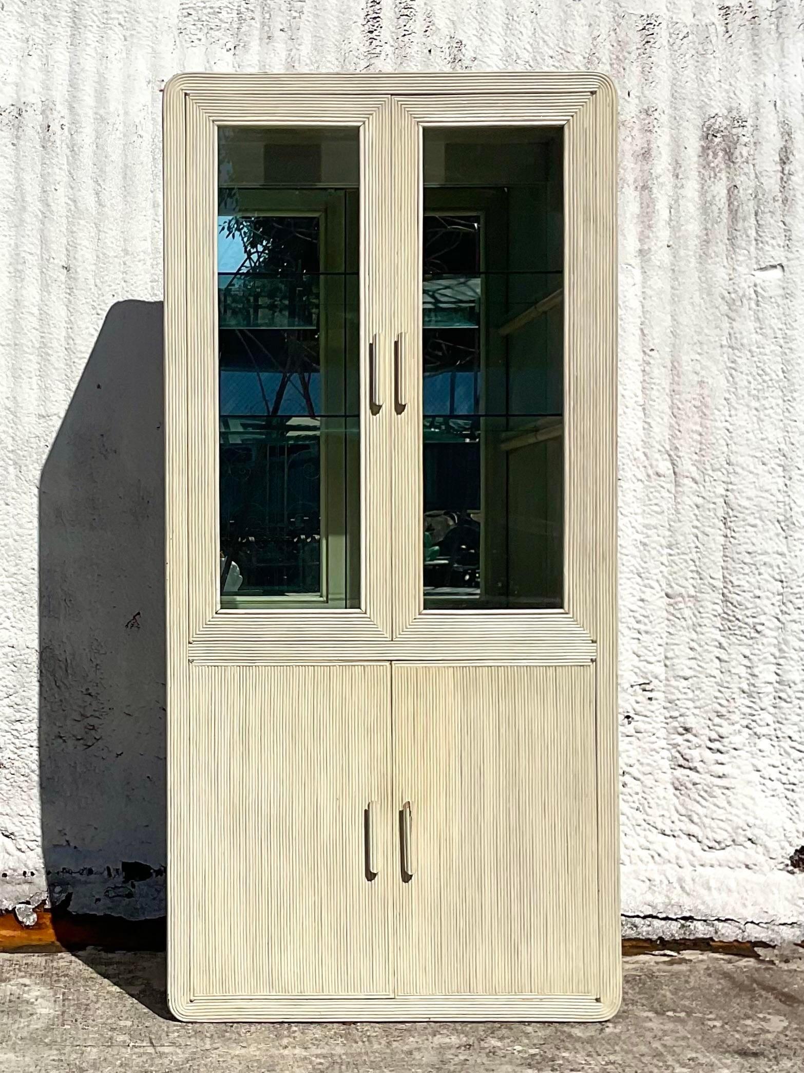 A fabulous vintage Coastal storage cabinet. A chic cerused pencil reed with a stone colored matte finish. Inset glass doors and interior upper glass shelves. Lots of great storage below. Acquired from a Palm Beach estate.