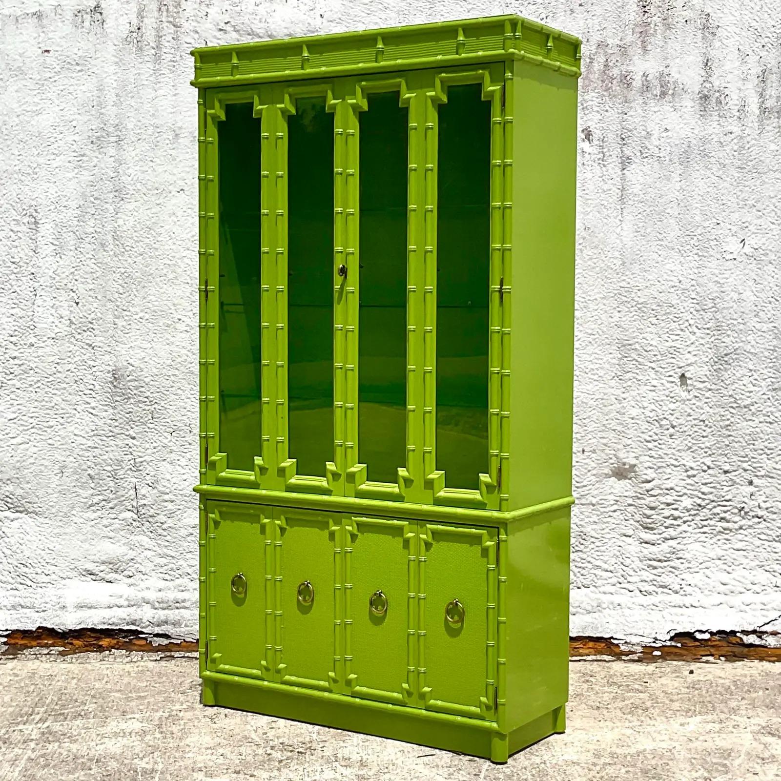 Fantastic vintage coastal China cabinet. A beautiful pea green lacquered finish on a chic bamboo trim design. Long glass doors and interior glass shelving. Acquired from a Palm Beach estate.