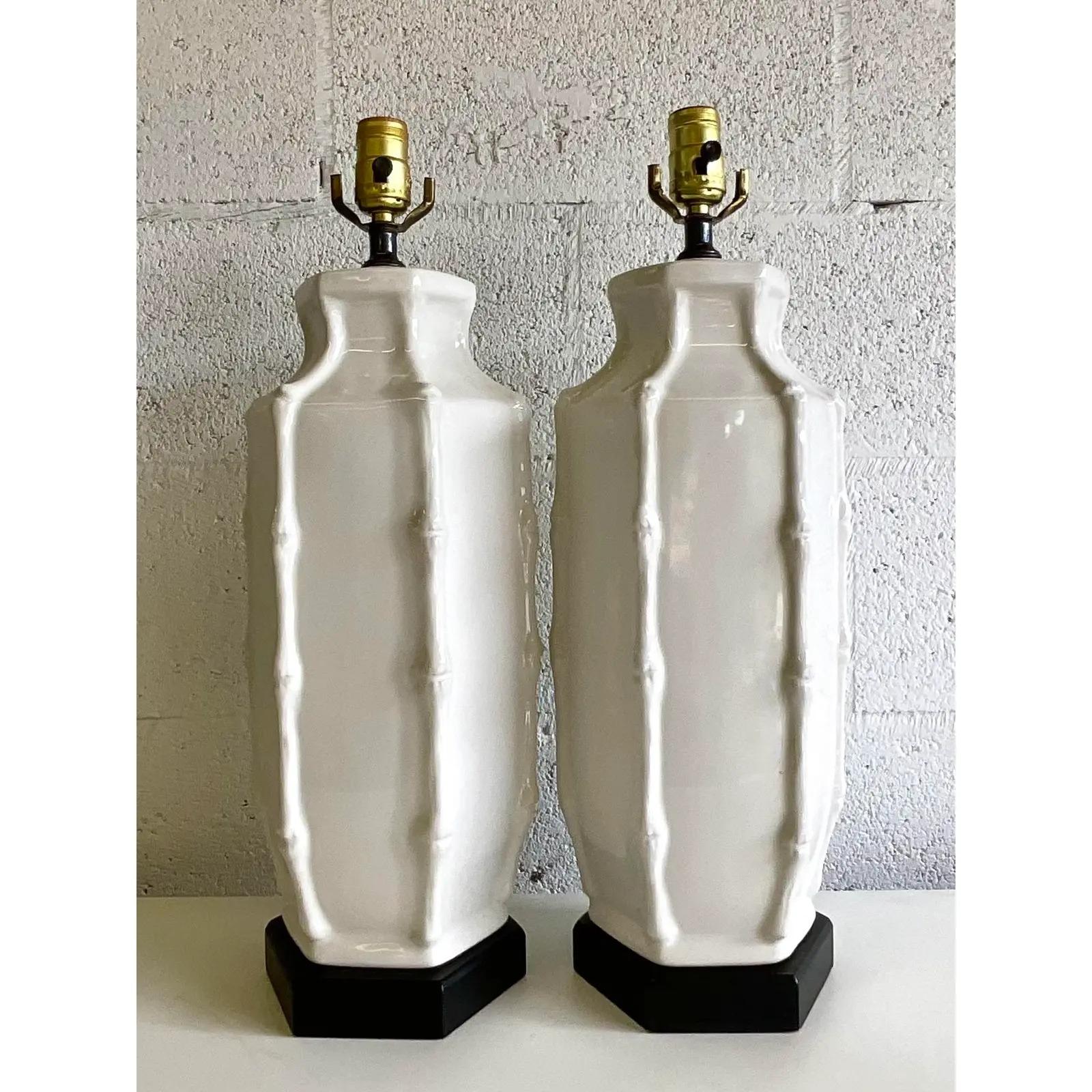 Gorgeous pair of vintage MCM glazed ceramic table lamps. Faux bamboo trim and a bright white finish. Rest on black wooden plinths. Acquired from a Palm Beach estate.