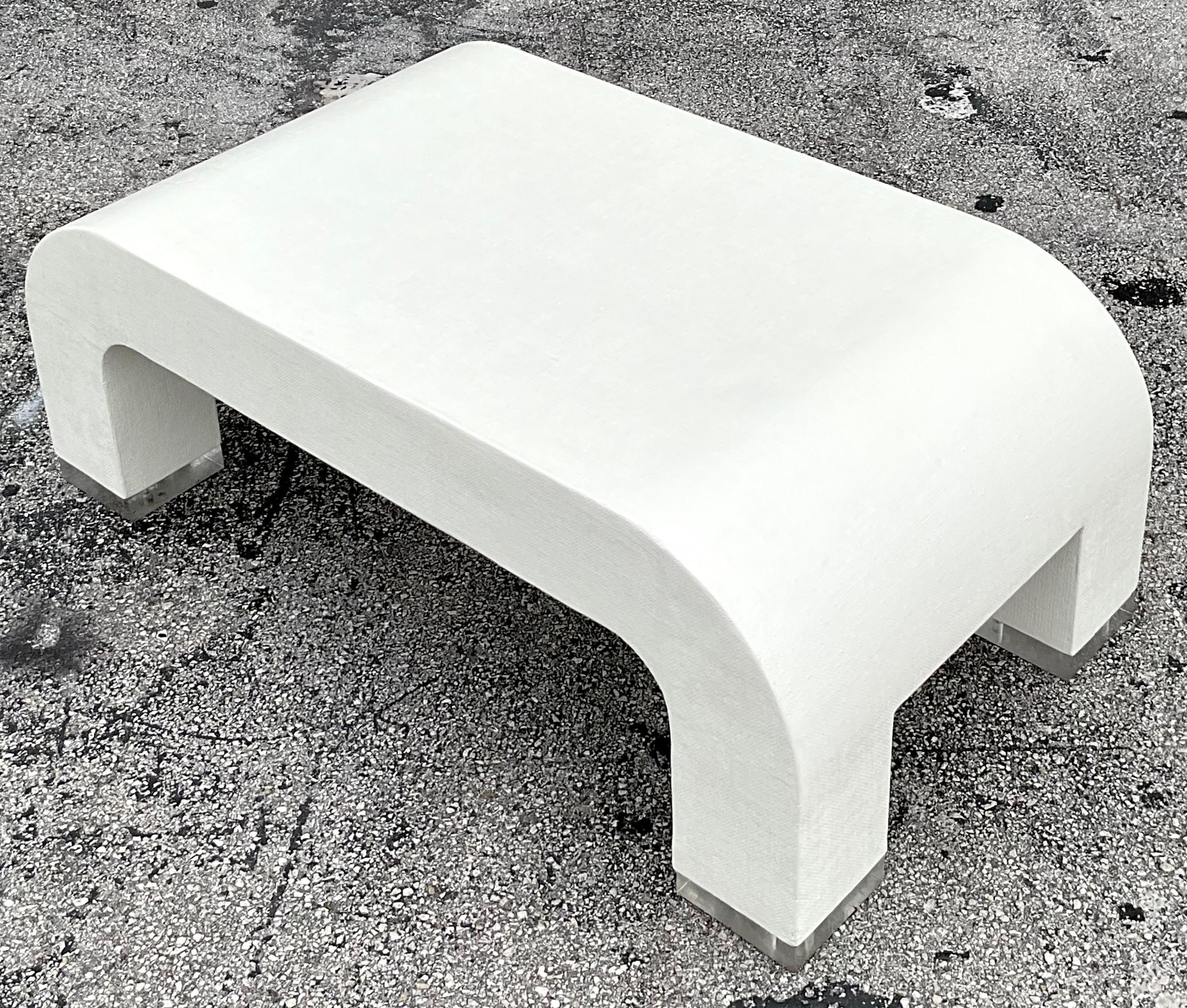 Elevate your living space with the Vintage Coastal Grasscloth and Lucite Waterfall Coffee Table, a perfect blend of coastal charm and modern elegance. This stunning piece features a sleek Lucite waterfall design, complemented by the natural texture