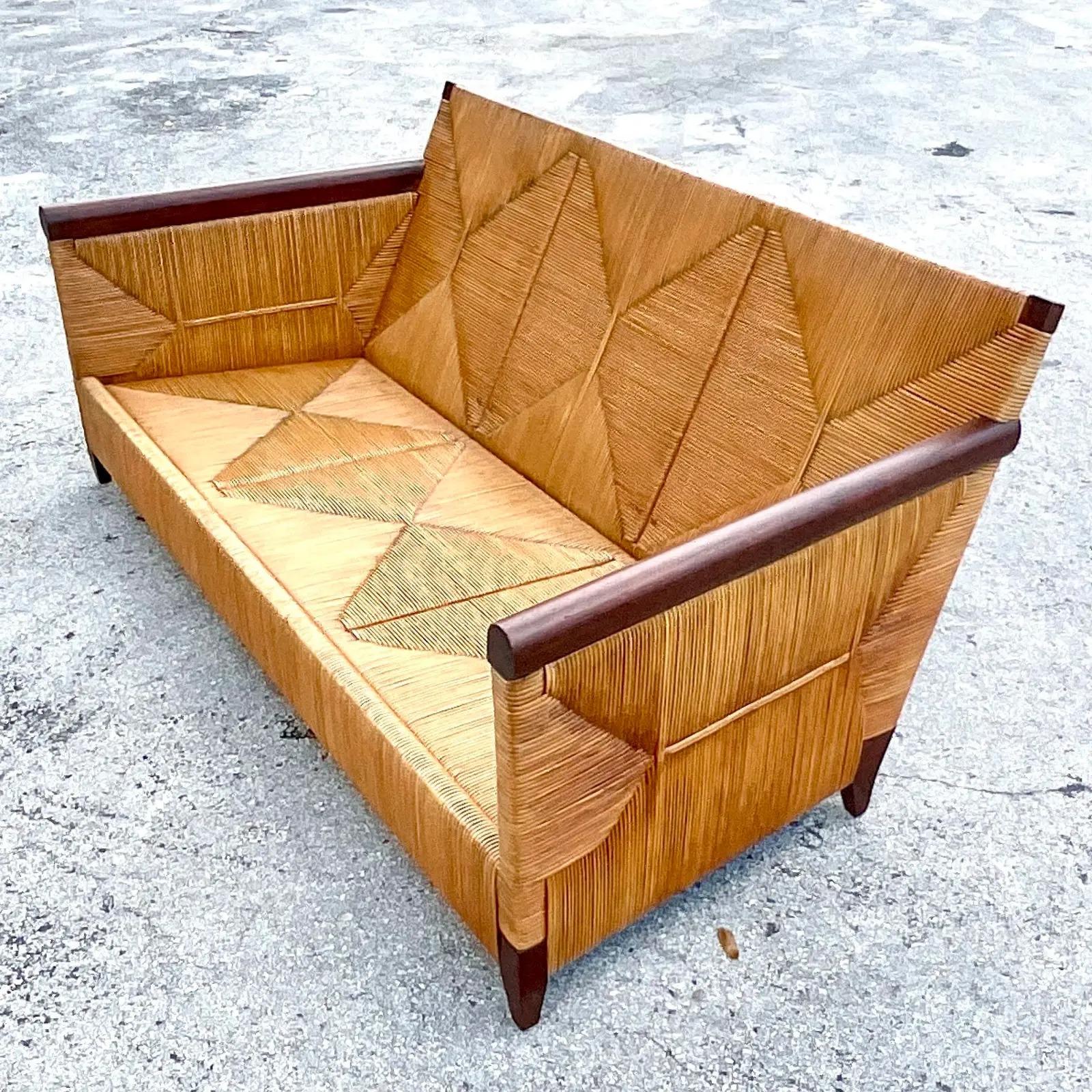 Fantastic vintage Coastal sofa. Designed by John Hutton for Donghia. Part of the coveted Merbau collection. Beautiful wood trimmed detail with a warm rattan body. Tagged on the bottom. Stained Mahogany arms and feet.