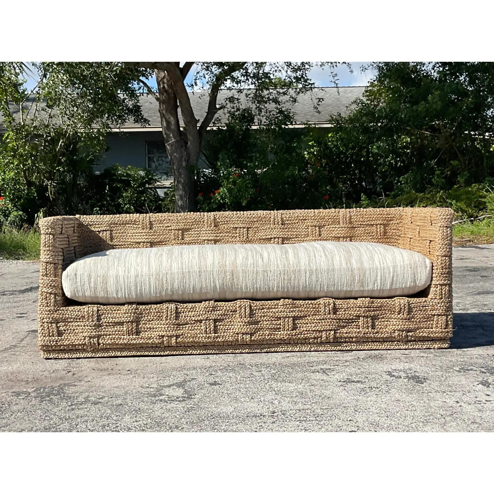 An outstanding vintage Coastal sofa. A chic woven sisal in an over under design a big down cushion upholstered in tan and white slub stripe. Acquired from a Palm Beach estate.