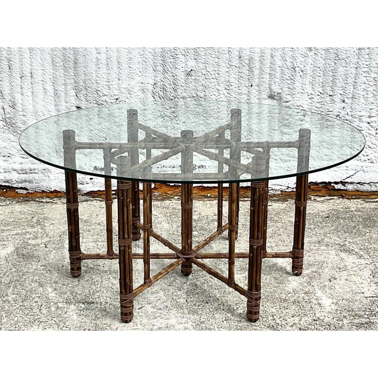 A fantastic vintage Coastal dining table. Made by the iconic McGuire group. Beautiful bundled rattan in a rich brown color. Thick glass top. Acquired from a Palm Beach estate.