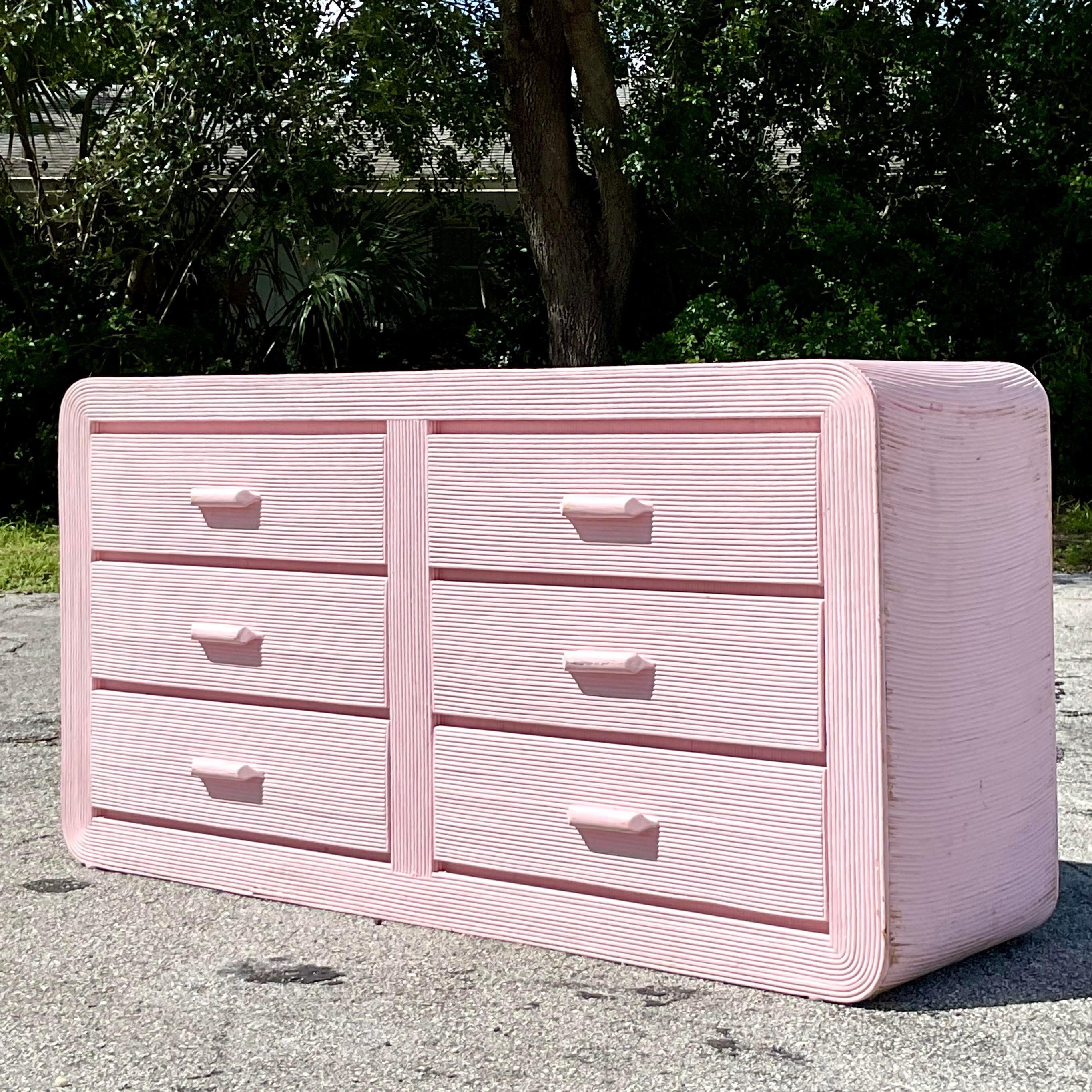 Add a soft, beachy elegance to your space with this Vintage Coastal Pale Pink Pencil Reed Waterfall Dresser. Featuring a gracefully curved waterfall silhouette, this dresser is beautifully wrapped in delicate pencil reed, giving it a natural,