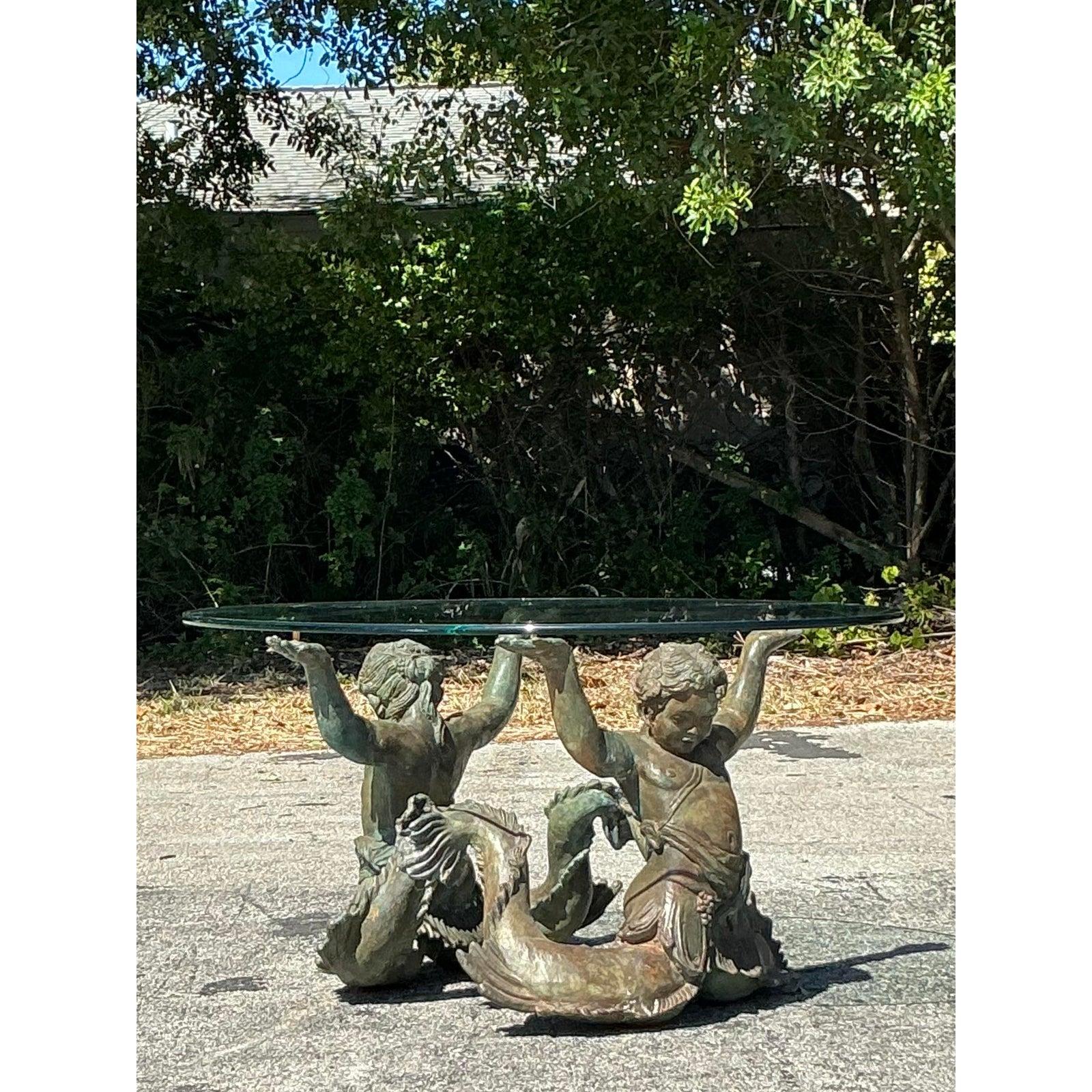 Élevez votre espace de vie avec cette exquise table basse côtière vintage, une fusion étonnante de l'art et de la fonction. Cette pièce unique présente deux Putti De Mare - des chérubins mythiques inspirés de la mer - fabriqués en bronze patiné