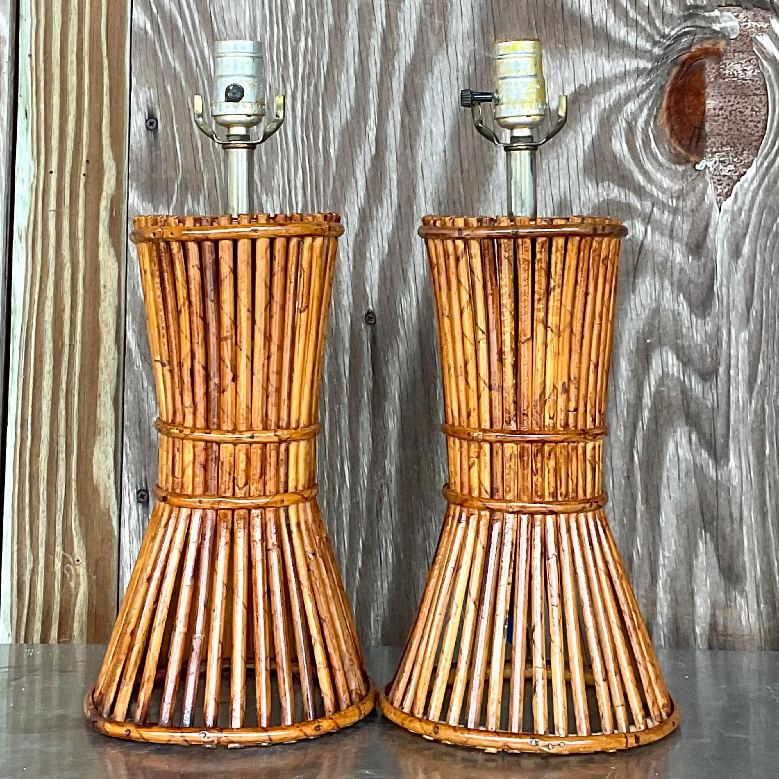 A fabulous pair of vintage Coastal table lamps. A chic pencil reed cylinder that is gathered in the middle. Woven rattan tops. Acquired from a Palm Beach estate.