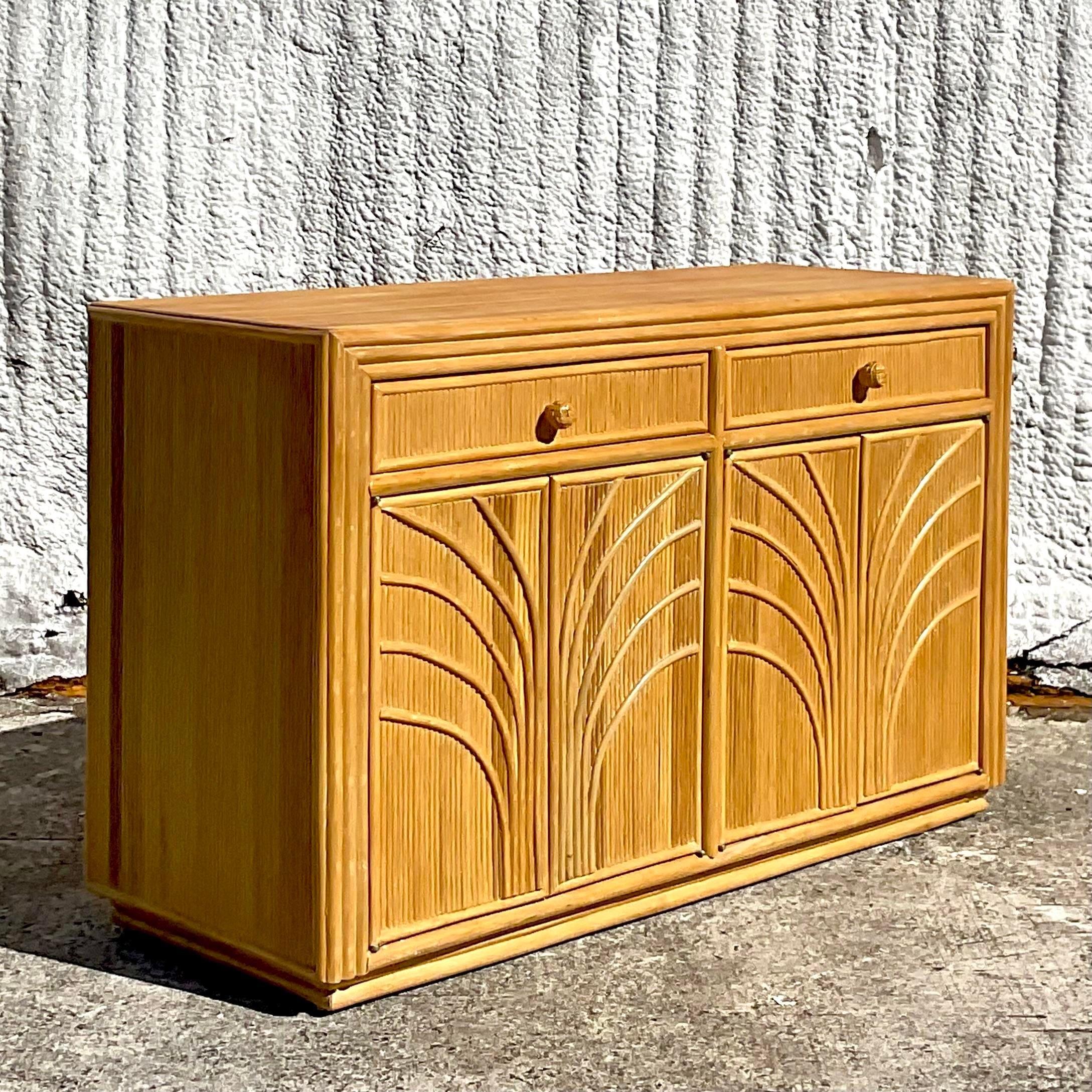 A fabulous vintage Coastal sideboard. A chic pencil reed cabinet with the iconic Palm Tree design on the door fronts. Lots of great interior storage and two drawers. Acquired from a Palm Beach estate.