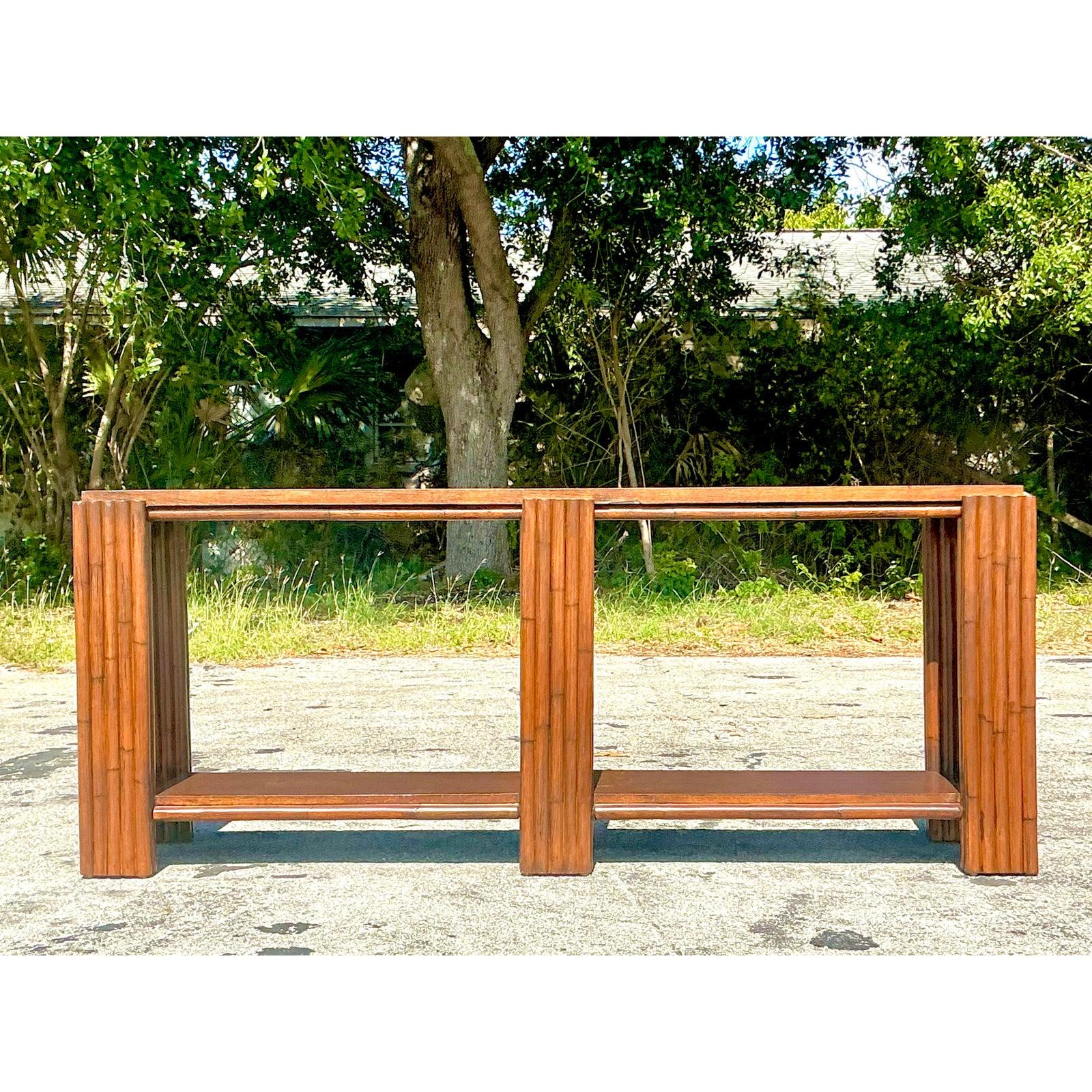 Add a touch of coastal charm and organic elegance to your space with this stunning vintage rattan console table. The rich honey-toned bamboo-style wood frame exudes tropical sophistication, while the sleek silhouette and open shelving lend a sense