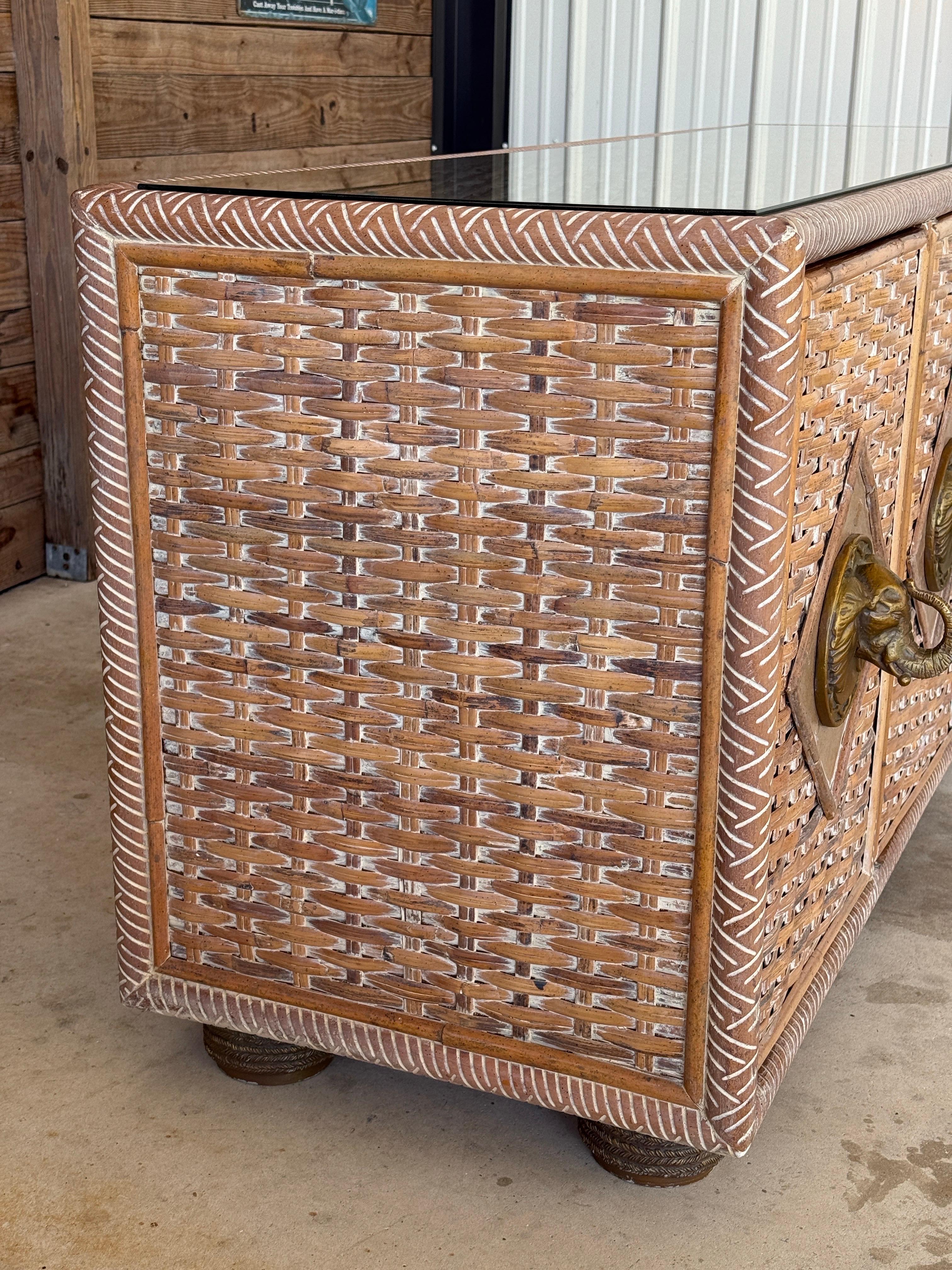 Statement-making and full of character, this vintage rattan and bamboo sideboard features a handwoven body with whitewashed detailing and sculptural brass elephant head pulls at the center of each door.
The cabinet opens to reveal spacious storage