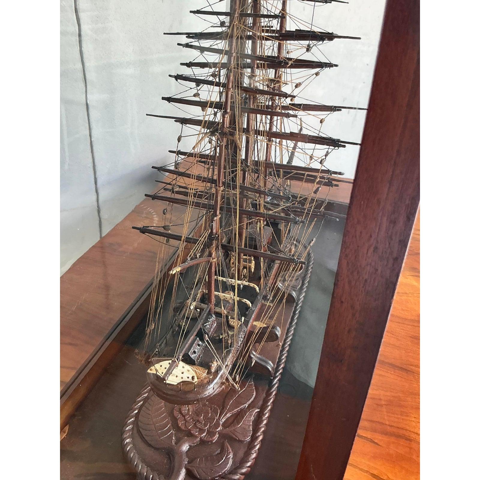 Parti per un viaggio con questo squisito modello di nave d'epoca in scala, meticolosamente realizzato a mano e presentato in una sofisticata teca di mogano e vetro. Questo pezzo cattura il fascino senza tempo della storia marittima, con sartiame