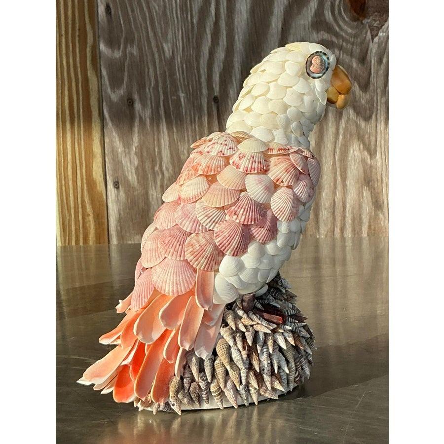 Questo affascinante uccello vintage incrostato di conchiglie è un delizioso esempio di arte costiera. Intricatamente ornato da una varietà di conchiglie nei toni tenui del bianco, del rosa e del pesca, questo pezzo irradia bellezza naturale e