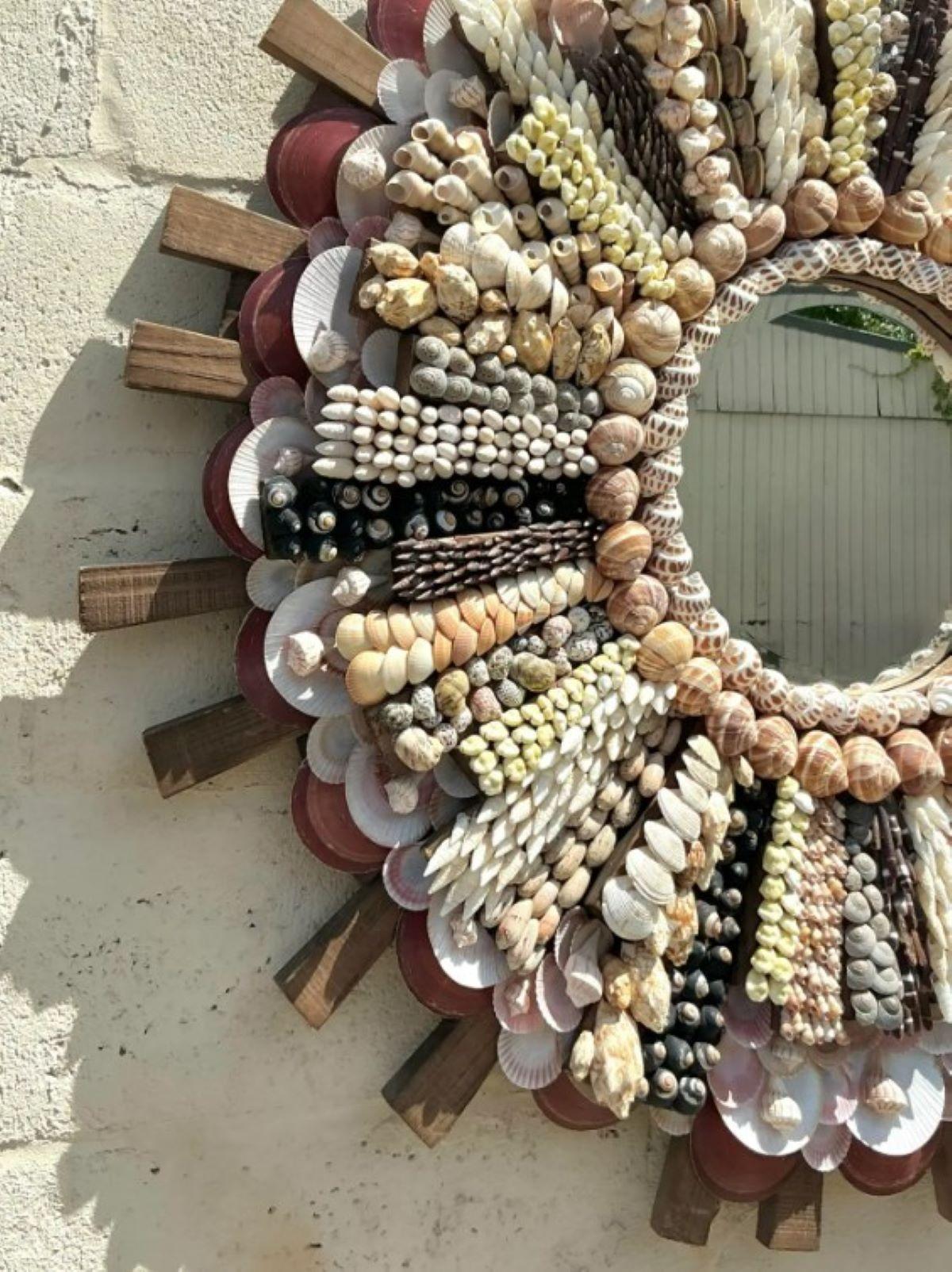 Lleva un toque marino a tu hogar con este impresionante espejo costero vintage, profusamente incrustado con un conjunto de conchas naturales dispuestas en un fascinante diseño de rayos de sol. Irradiando encanto costero y artesanía, este espejo