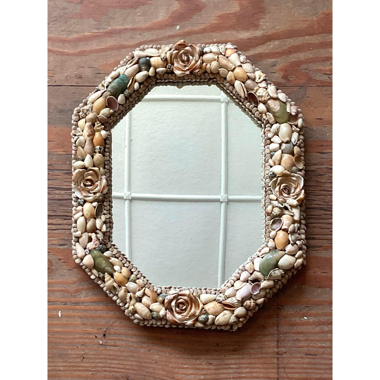 Questo affascinante specchio vintage è un perfetto esempio di artigianato coastal chic e bohémien. La cornice ottagonale è meticolosamente incrostata con un mosaico di conchiglie naturali, che variano in dimensioni e tonalità per creare un arazzo