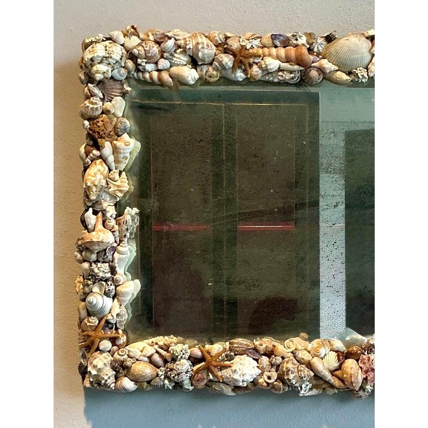 Evoca la serena bellezza del mare con questo affascinante specchio vintage tempestato di conchiglie. Questo pezzo squisito cattura l'essenza della vita costiera, con una serie di conchiglie naturali applicate meticolosamente a mano in varie forme,