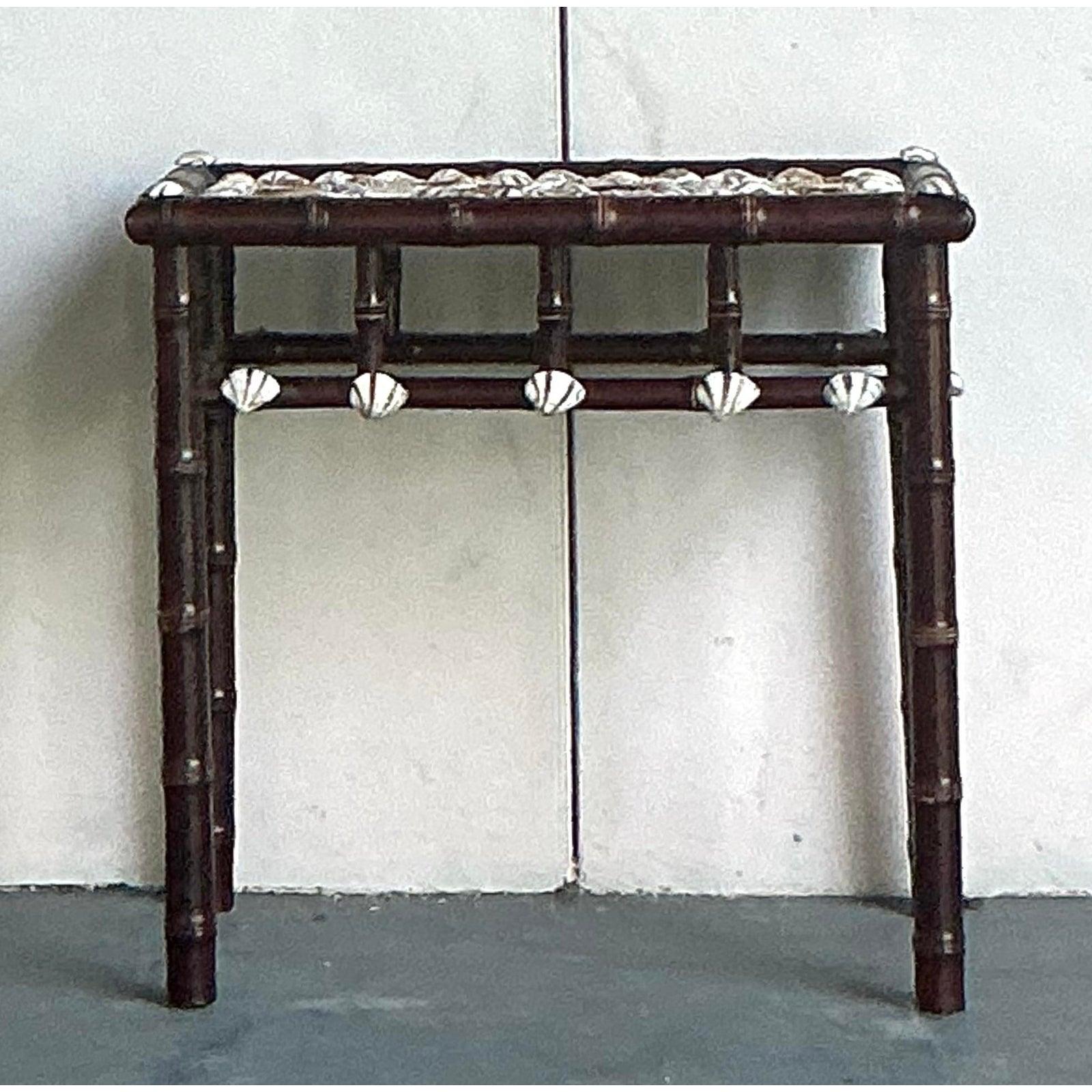 Evoke the serene beauty of the seaside with this charming Vintage Coastal Shell Encrusted Bamboo Side Table. This unique piece captures the essence of coastal living with its meticulously arranged shell inlay tabletop, featuring a captivating array