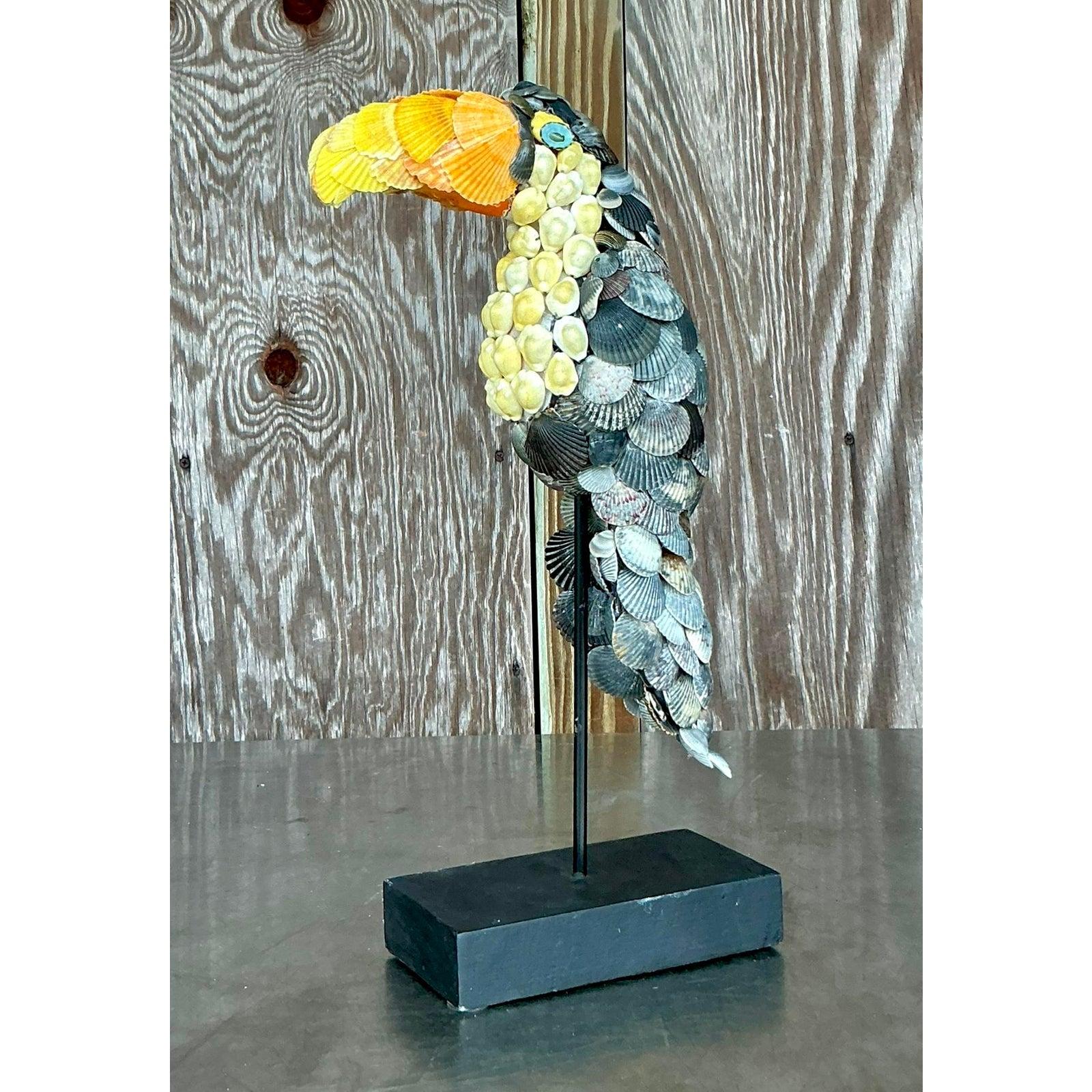 Cattura l'essenza del fascino costiero e dell'estro tropicale con questa deliziosa scultura vintage di tucano. Sapientemente realizzato a mano, questo pezzo unico presenta una vivace figura di tucano meticolosamente incrostata con una serie di