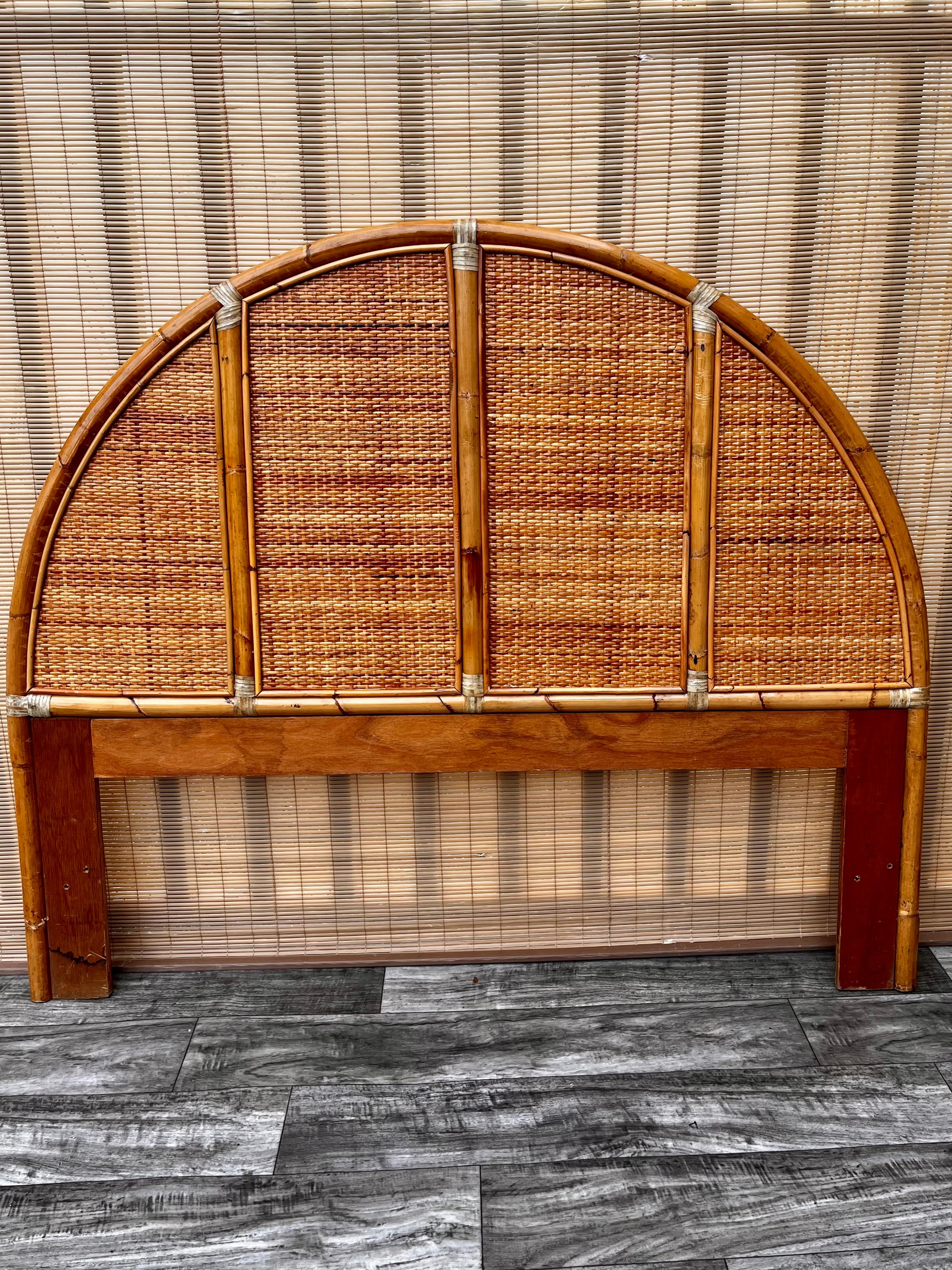 Vintage Boho Chic / Coastal Style Arched Rattan Queen Headboard in the McGuire's Style. circa 1980s.
Features a gracefully arched rattan frame with four woven cane panels and leather straps.
In excellent original condition with very minor signs of