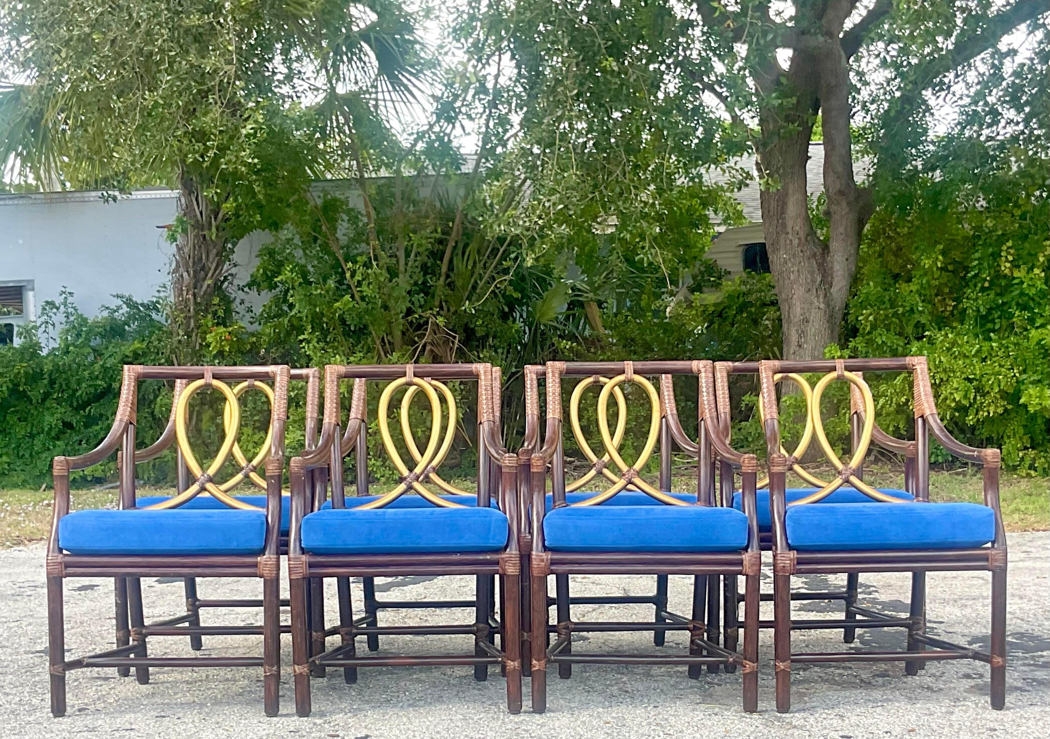 A stunning set of 8 vintage Coastal dining chairs. Made by the iconic McGuire group and tagged on the bottom. A brilliant coffee rattan finish with a gilt loop detail. A brilliant blue cushion provides a flash of color. Acquired from a Palm Beach