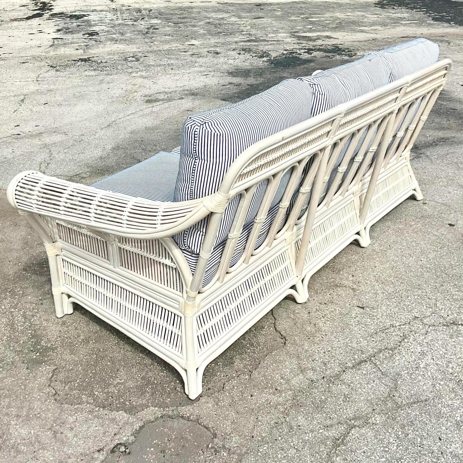 Fabulous vintage coastal sofa. A beautiful bent rattan in a white finish with chic ticking stripe upholstery. Ready to glam up your sunroom or summer house. Acquired from a Palm Beach estate.