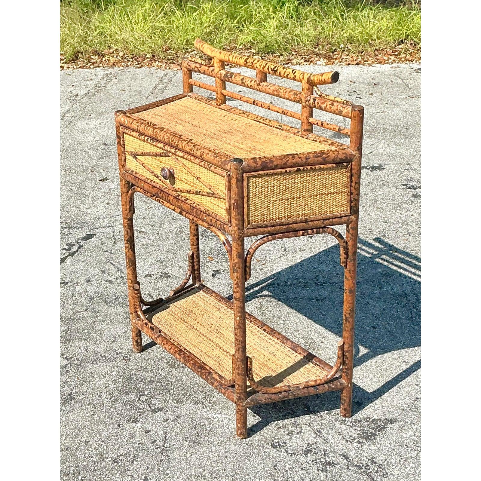 Questo squisito tavolo consolle vintage presenta una straordinaria struttura in bambù tartarugato e una superficie in rattan splendidamente intrecciata, che incarna una miscela perfetta di texture organiche ed eleganza costiera. Il suo