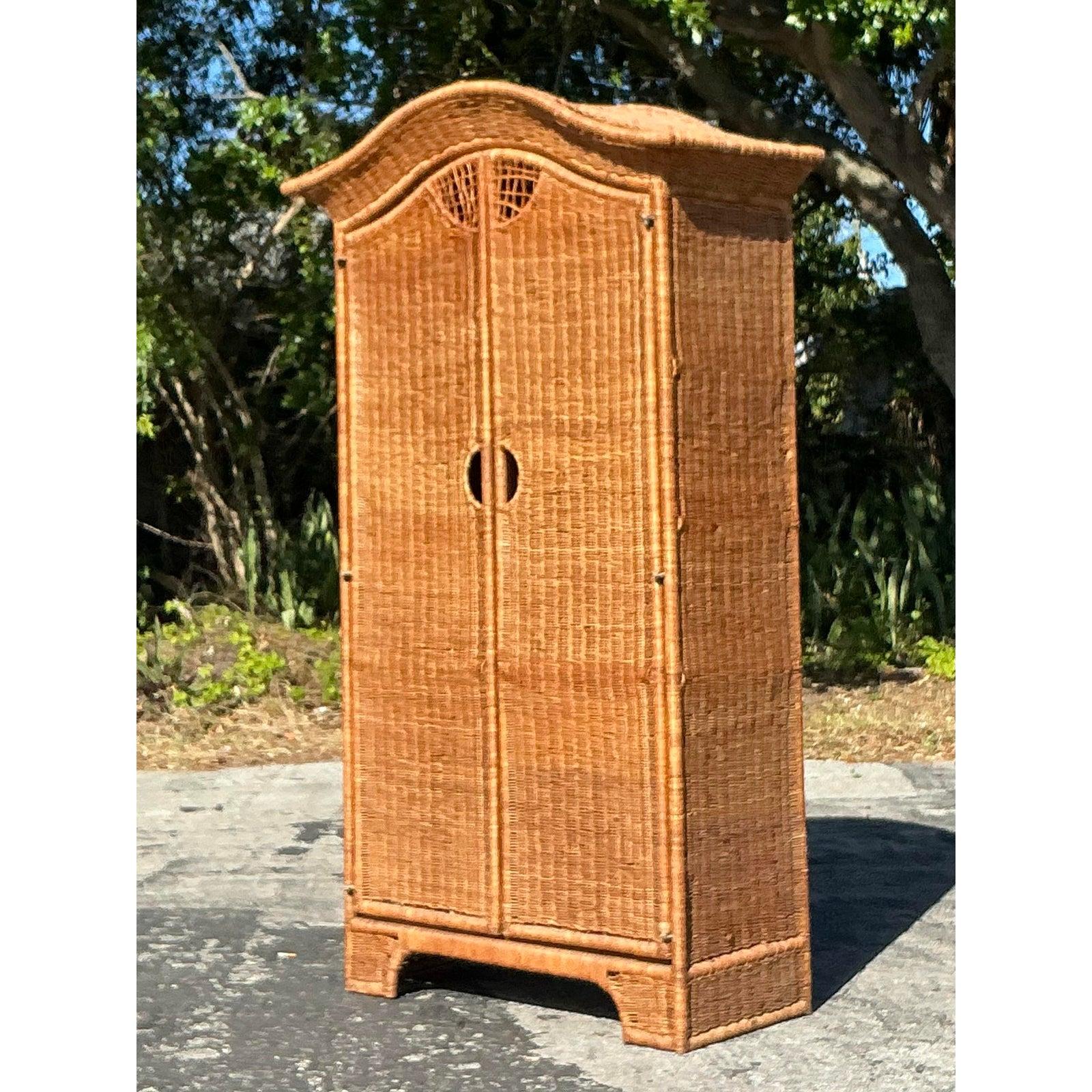 Dai un tocco di fascino costiero alla tua casa con questo splendido armadio vintage in rattan intrecciato. Caratterizzato da un elegante piano ad arco e da dettagli finemente intrecciati, questo pezzo forte fonde texture naturali e artigianato senza