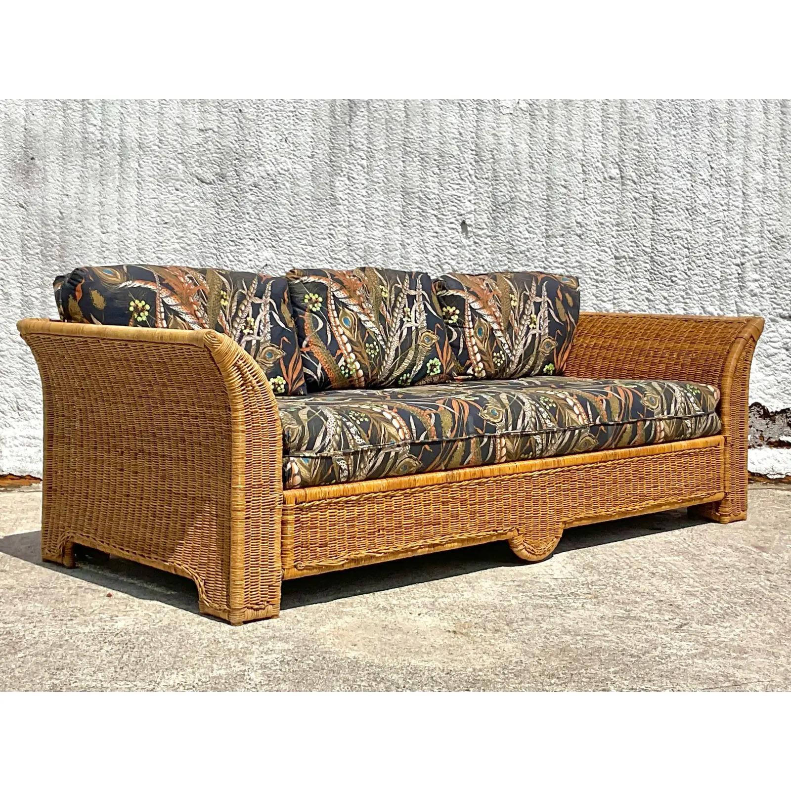 A fantastic vintage Coastal sofa. A chic woven rattan with a covered back and bat wing design. A printed polished cotton upholstery that’s in great shape. Acquired from a Palm Beach estate.