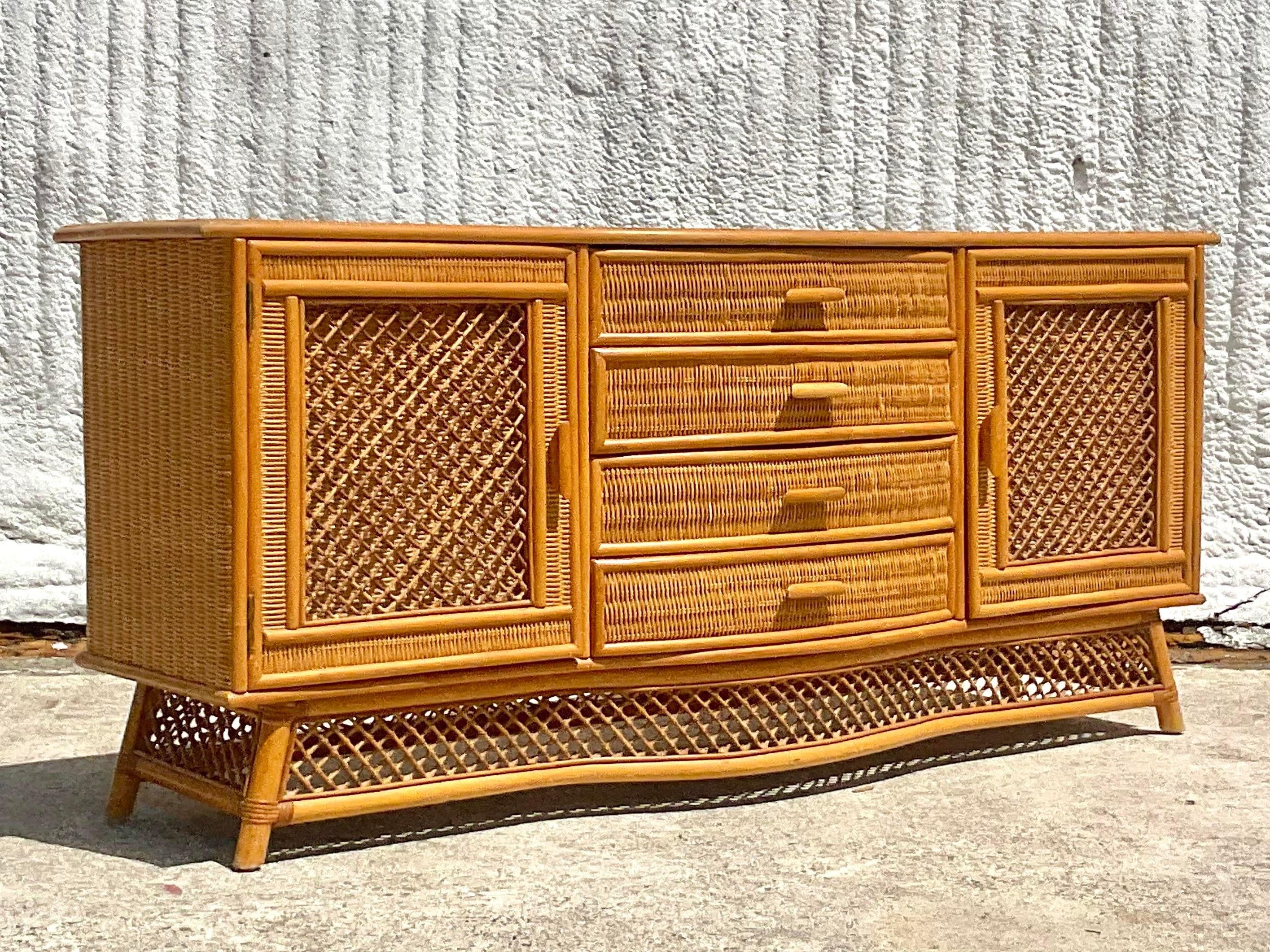 A stunning vintage Coastal woven rattan credenza. A chic bow front design with trellis detail on the door front and apron. Woven rattan top. Acquired from a Palm Beach estate.
