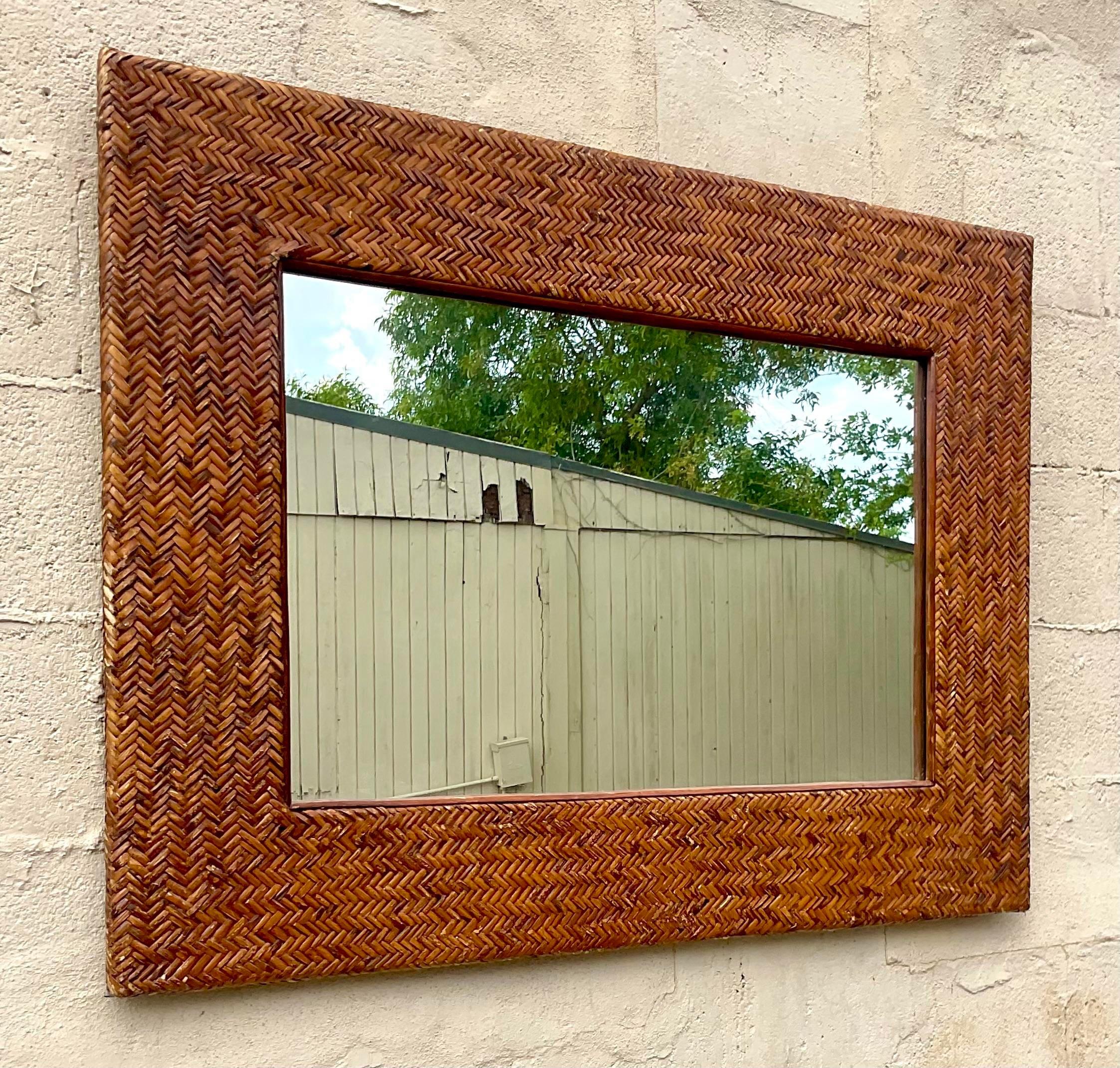 A fabulous vintage Coastal wall mirror. A chic woven rattan wide frame in a beautiful herringbone weave. Acquired from a Palm Beach estate. 