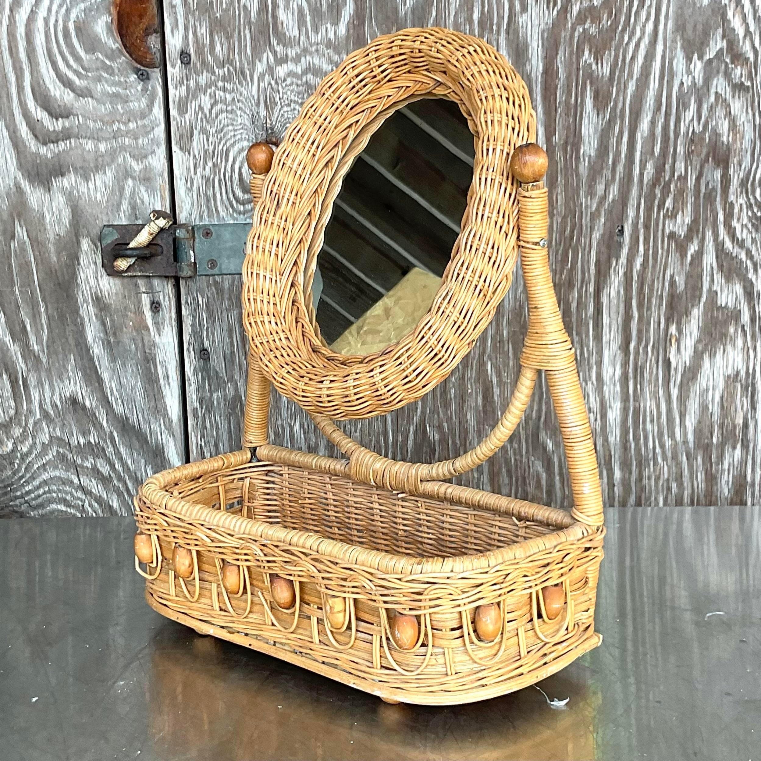 A fabulous little table top mirror. A chic woven rattan with a row of wooden beads for fun! A little attached basket for storage. Acquired from a Palm Beach estate.