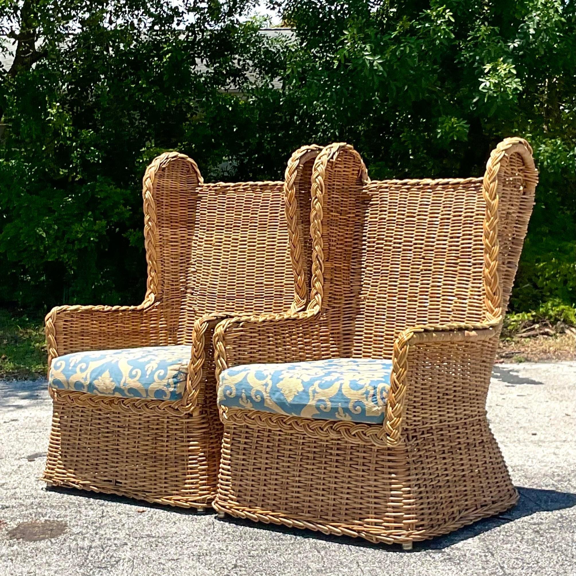 A spectacular pair of vintage Coastal Wingback chairs. Chic thick woven rattan in the iconic shape. Gorgeous braided rattan trim. Acquired from a Palm Beach estate.