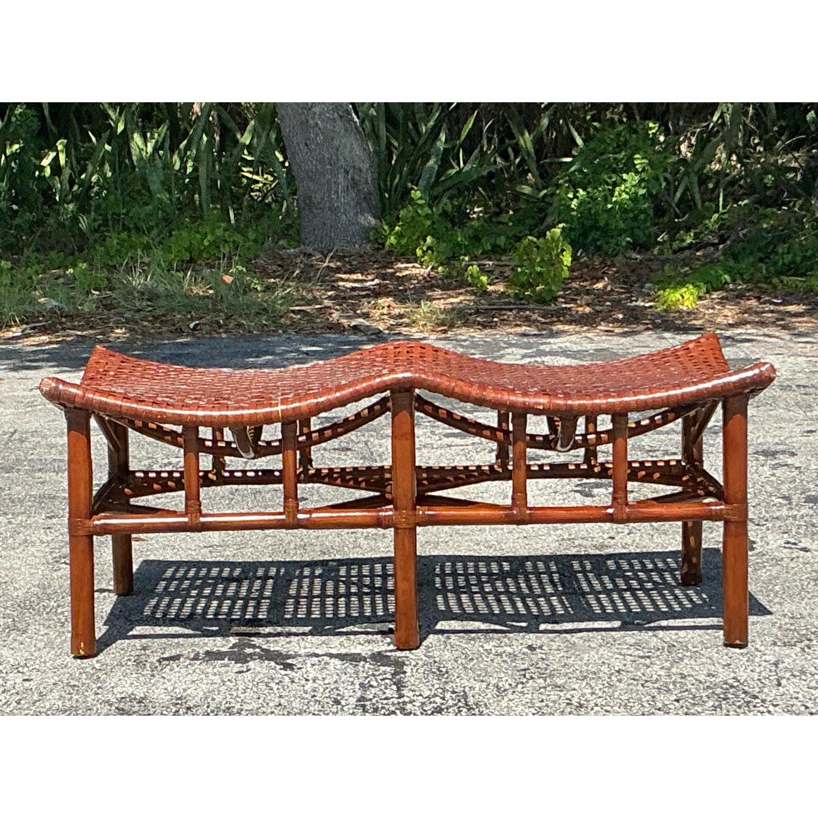 Ce banc côtier vintage présente une structure en rotin remarquable et une assise en cuir brut tissé de manière complexe, dans une élégante silhouette à double arche en 
