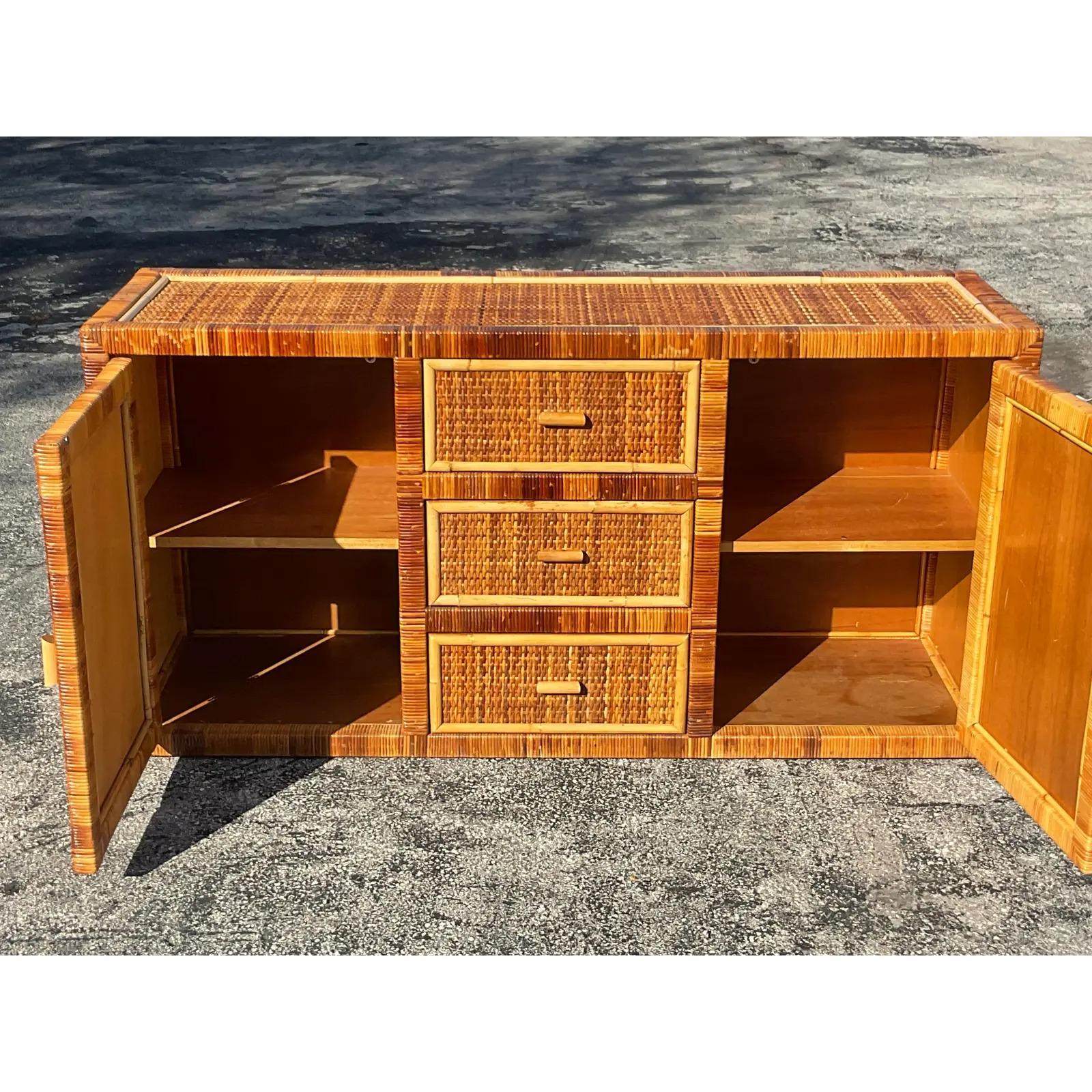 A fabulous vintage Coastal credenza. A chic wrapped rattan in rich warm colors. Lots of great storage below with two cabinets and three doors. Inset woven rattan panels. Acquired from a Palm Beach estate. 