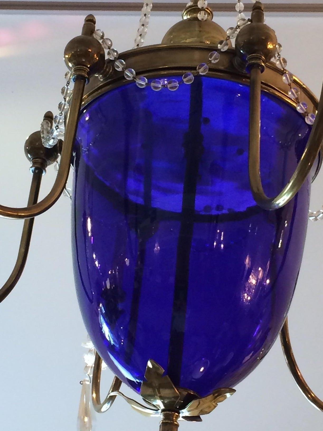 Auffällige und ungewöhnliche Leuchte mit einer großen zentralen Kuppel aus kobaltblauem Glas:: umgeben von sechs Messingarmen:: die mit großen Kristallprismen verziert sind. Das Oberteil ist mit filigranen Ketten aus Kristall geschmückt.   Blaues