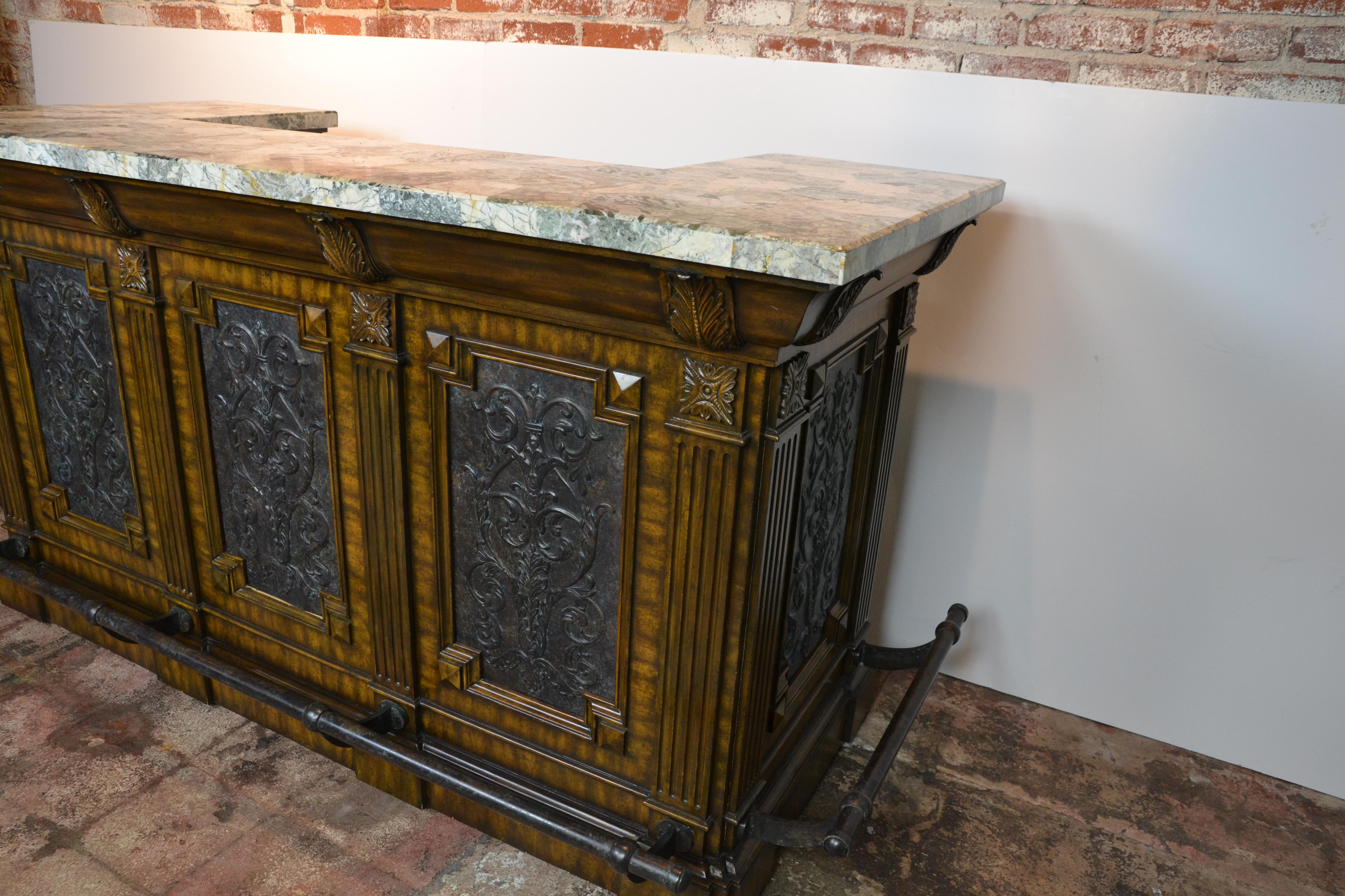 A vintage mahogany cocktail bar of really good quality. Pressed metal panels to the front and sides, decorated with Acanthus leaf designs. Panels have an aged patina. Foot rails are patinated like aged bronze. Drawers and cupboards to the reverse