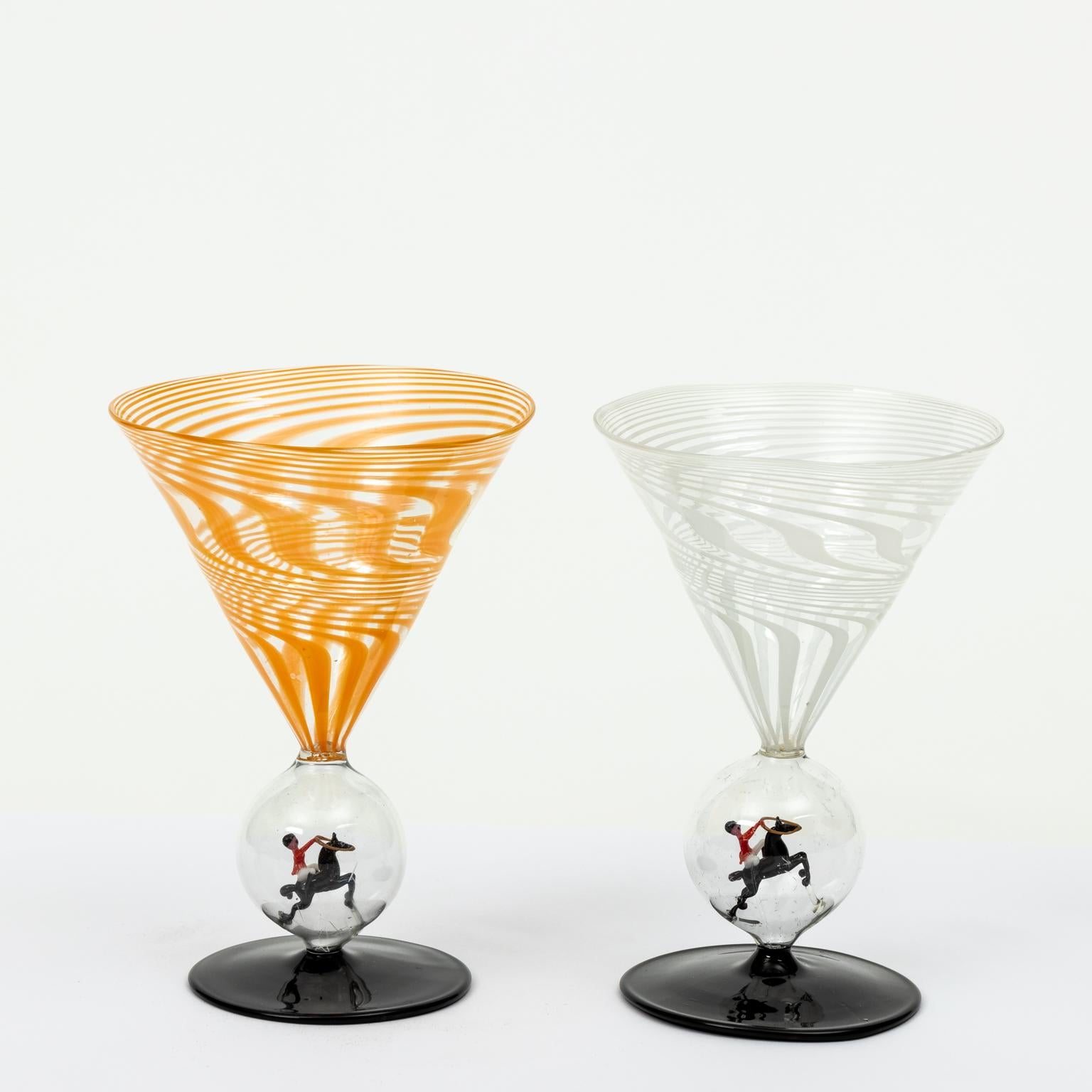 Circa 1920s-1930s set of two Bimini cocktail martini glasses with stirrers. The bowl of the glasses feature an orange and white swirl pattern, while the stems are decorated with capsules containing delicate horsemen figures. Made in Austria. Please