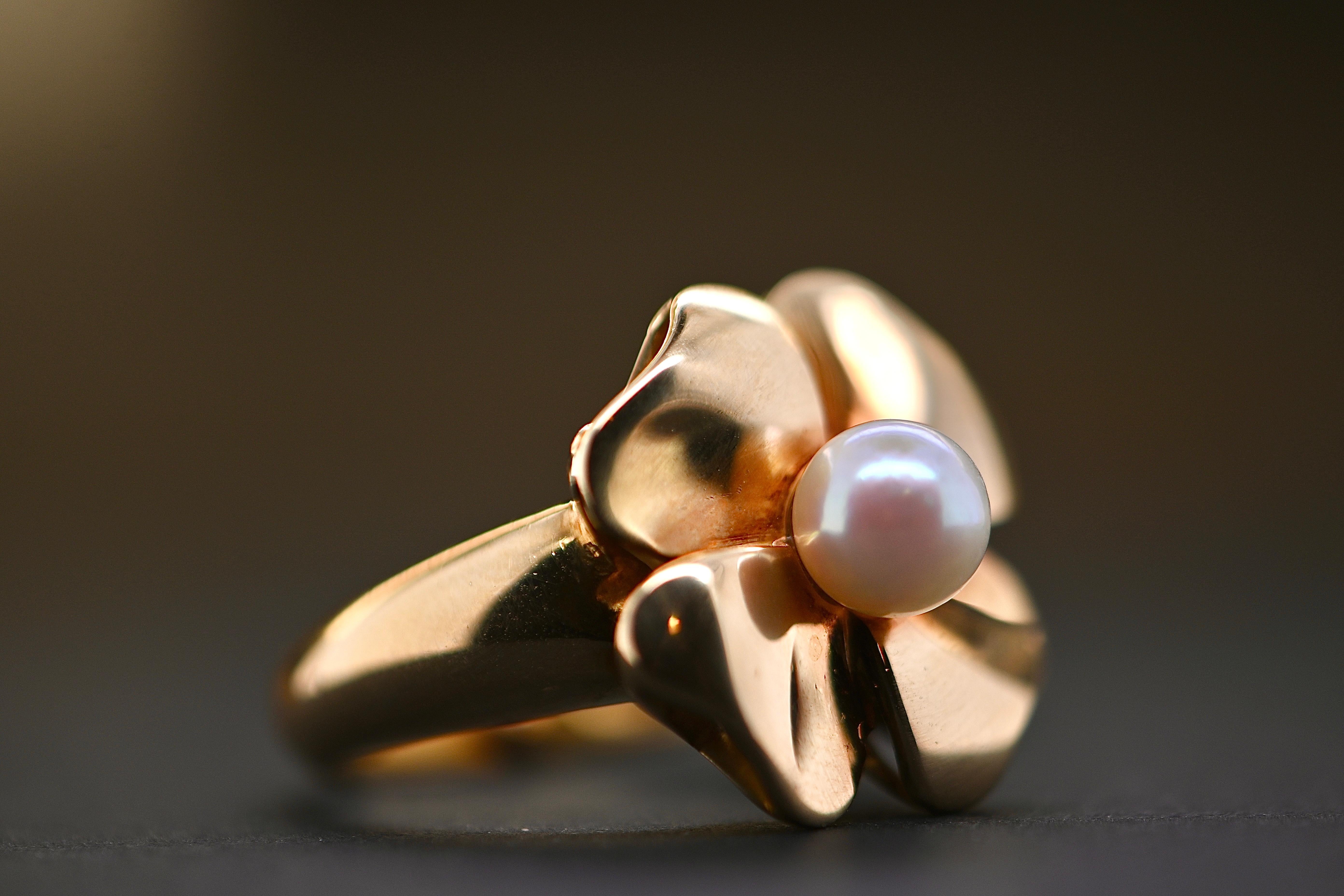 Dieser hübsche Ring aus den 1980er Jahren zeigt eine Blume oder ein vierblättriges Kleeblatt, das von einer Zuchtperle gekrönt wird. Sein schilfartiger Körper deckt den Finger gut ab. Dieses Juwel im Vintage-Stil wird Sie mit seiner Modernität