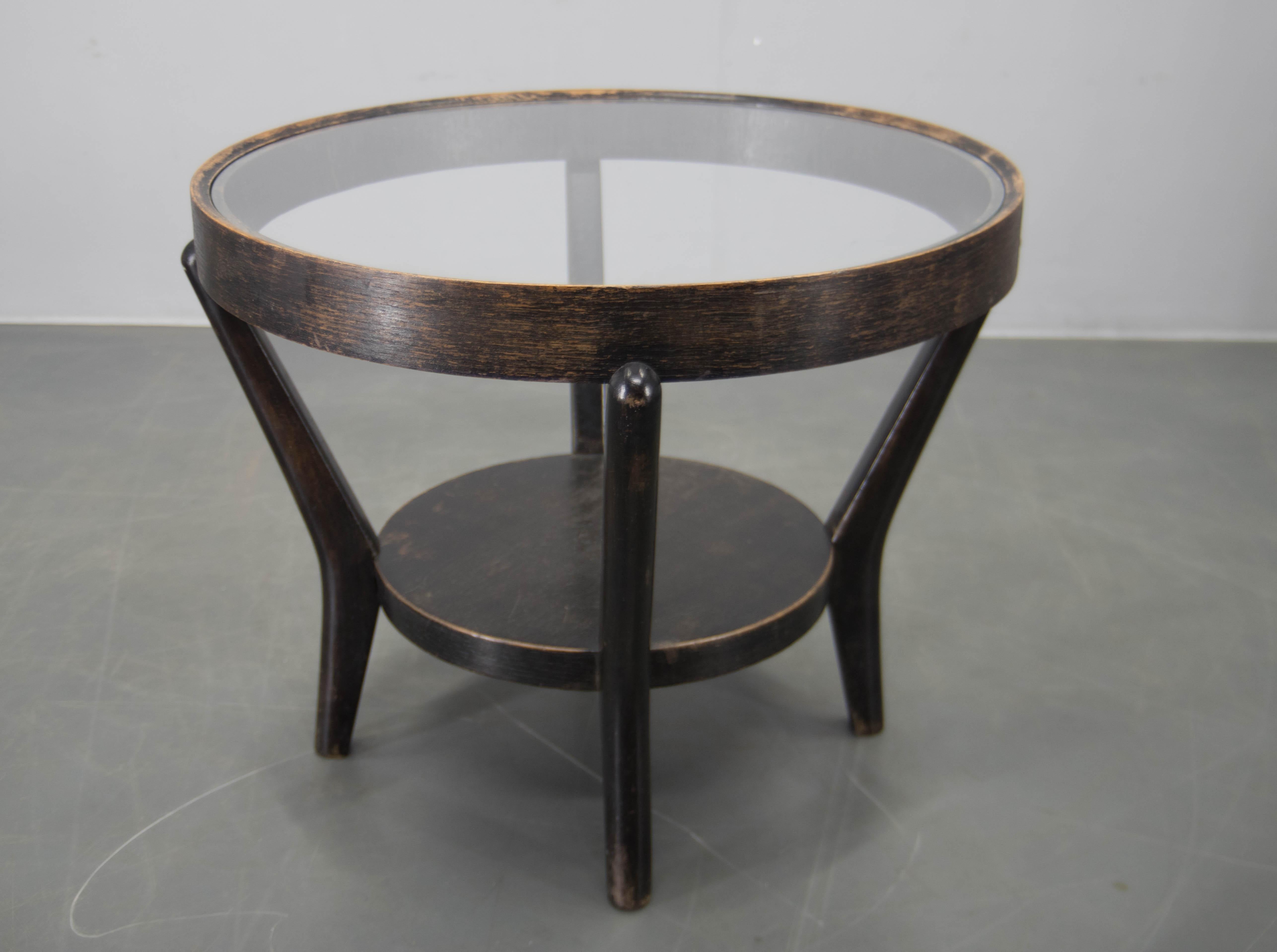 This iconic Mid-century coffee table by Czech designers Karel Kozelka and Antonín Kropáček features a distinctive bentwood frame with a round glass top and lower shelf. Originally designed in the 1940s, the piece reflects the elegant, modern lines