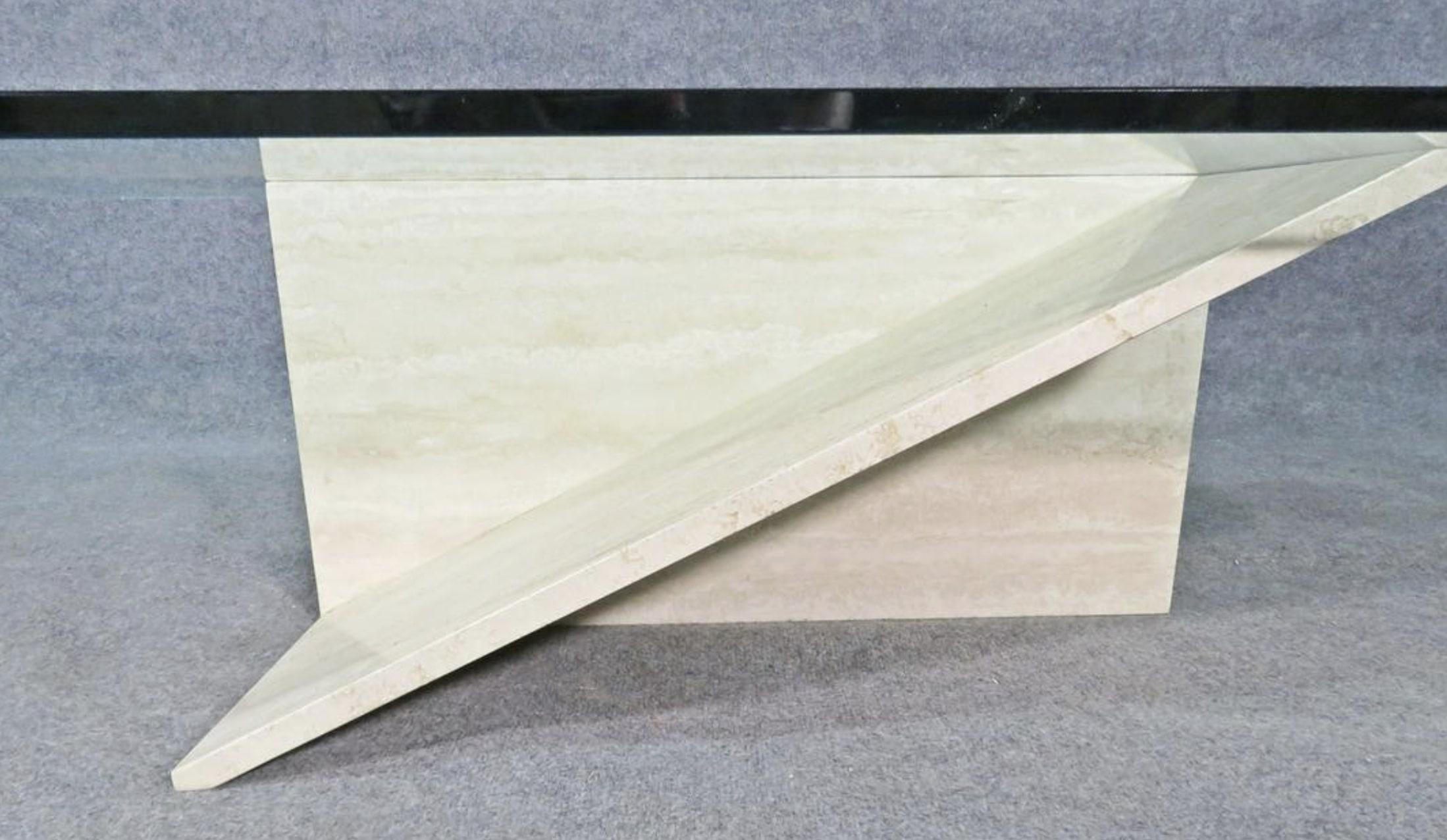 Cette impressionnante table basse combine une base géométrique en travertin avec un grand plateau en verre, faisant de cette table vintage un point focal unique de n'importe quelle pièce. Veuillez confirmer la localisation de l'objet auprès du