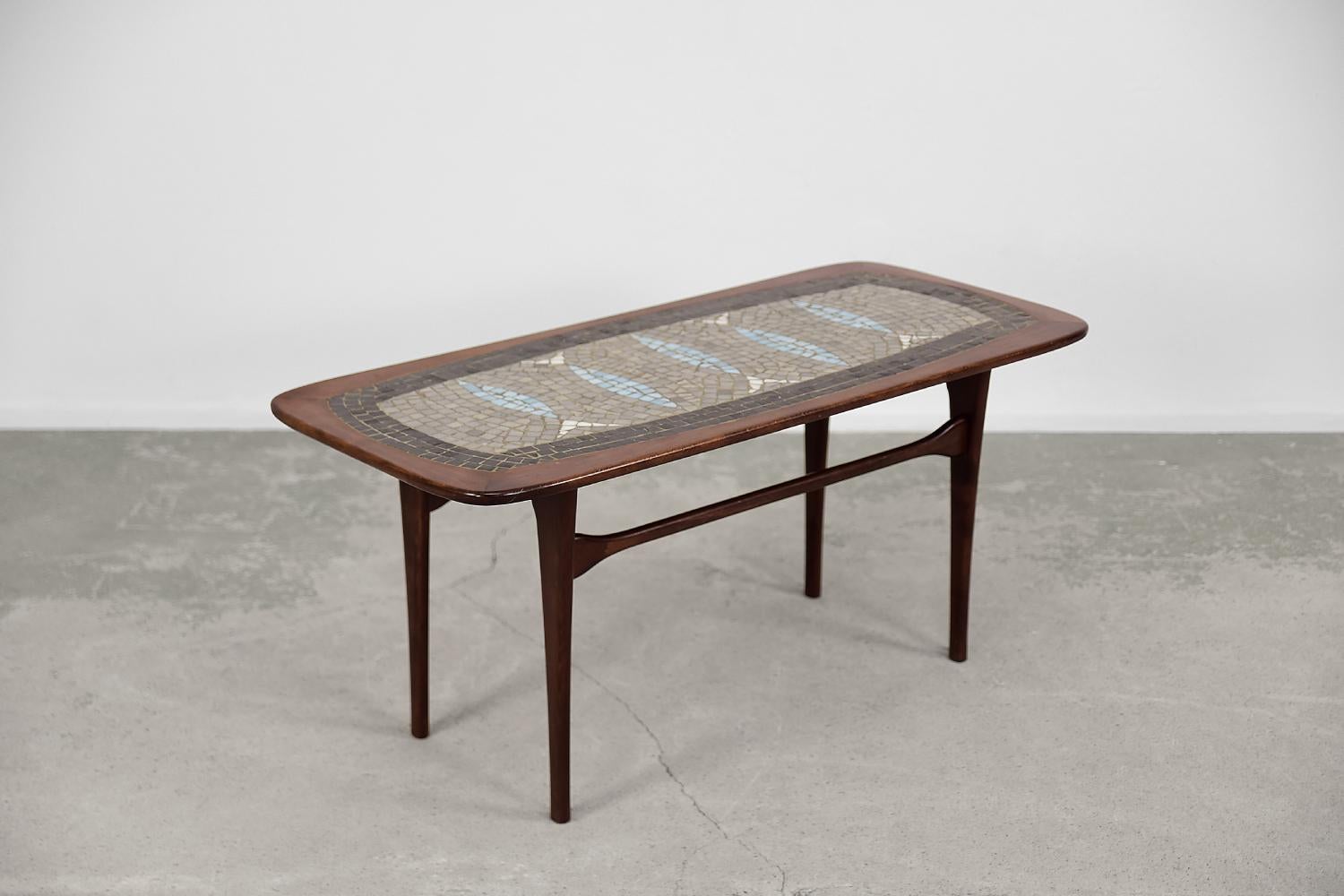 This coffee table was designed by Edvard Johansson for the Swedish manufacture Edvard Johansson Möbelfabrik during the 1960s. The table made of dark-colored beech wood. The tabletop is decorated with an inlaid mosaic of fish. Ceramic tesserae are