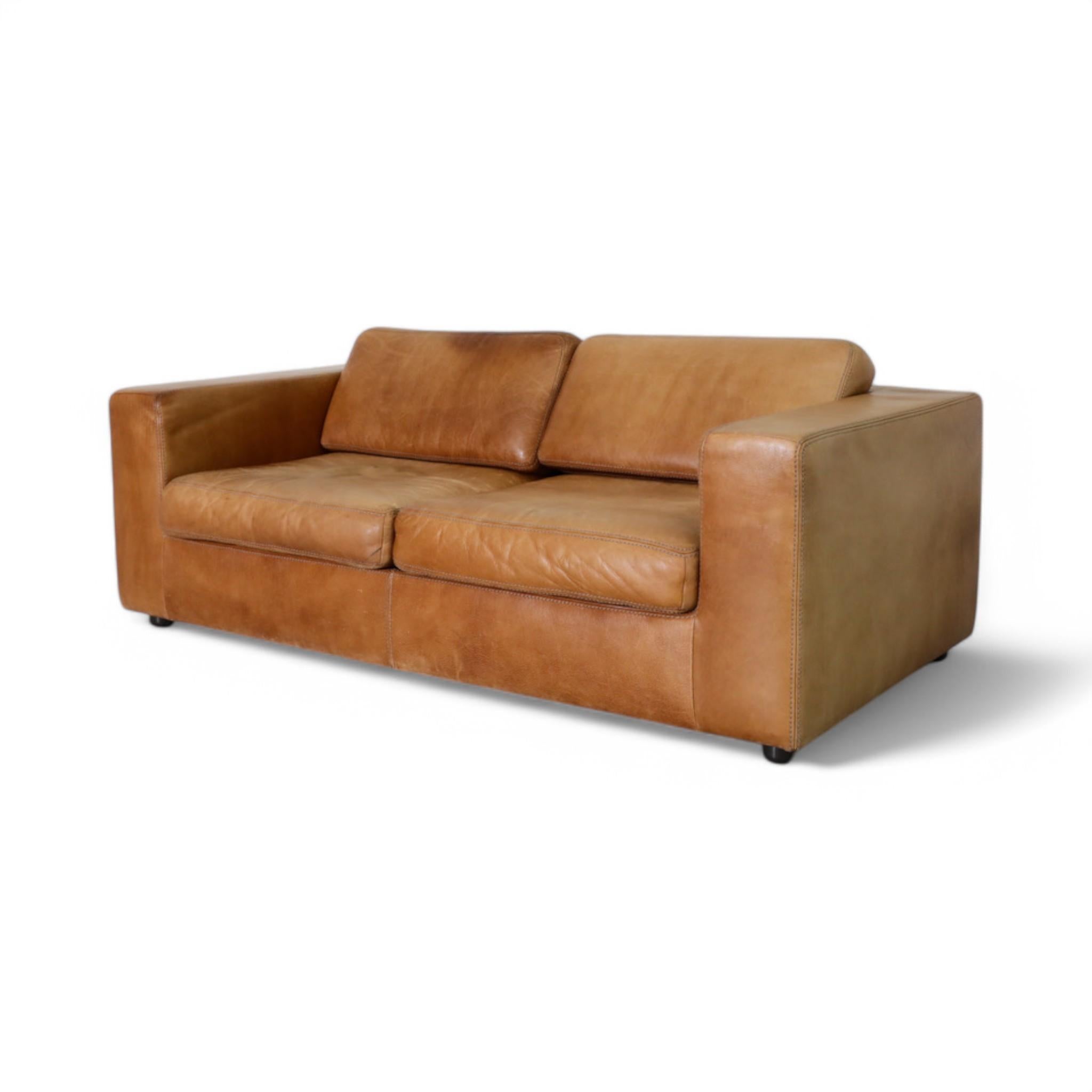 Fabriquée à la main en Belgique par Durlet, cette causeuse vintage en cuir cognac témoigne d'un savoir-faire de qualité et d'un design intemporel. Le cuir souple a développé une riche patine, ce qui ajoute à son caractère et à sa chaleur. Avec sa