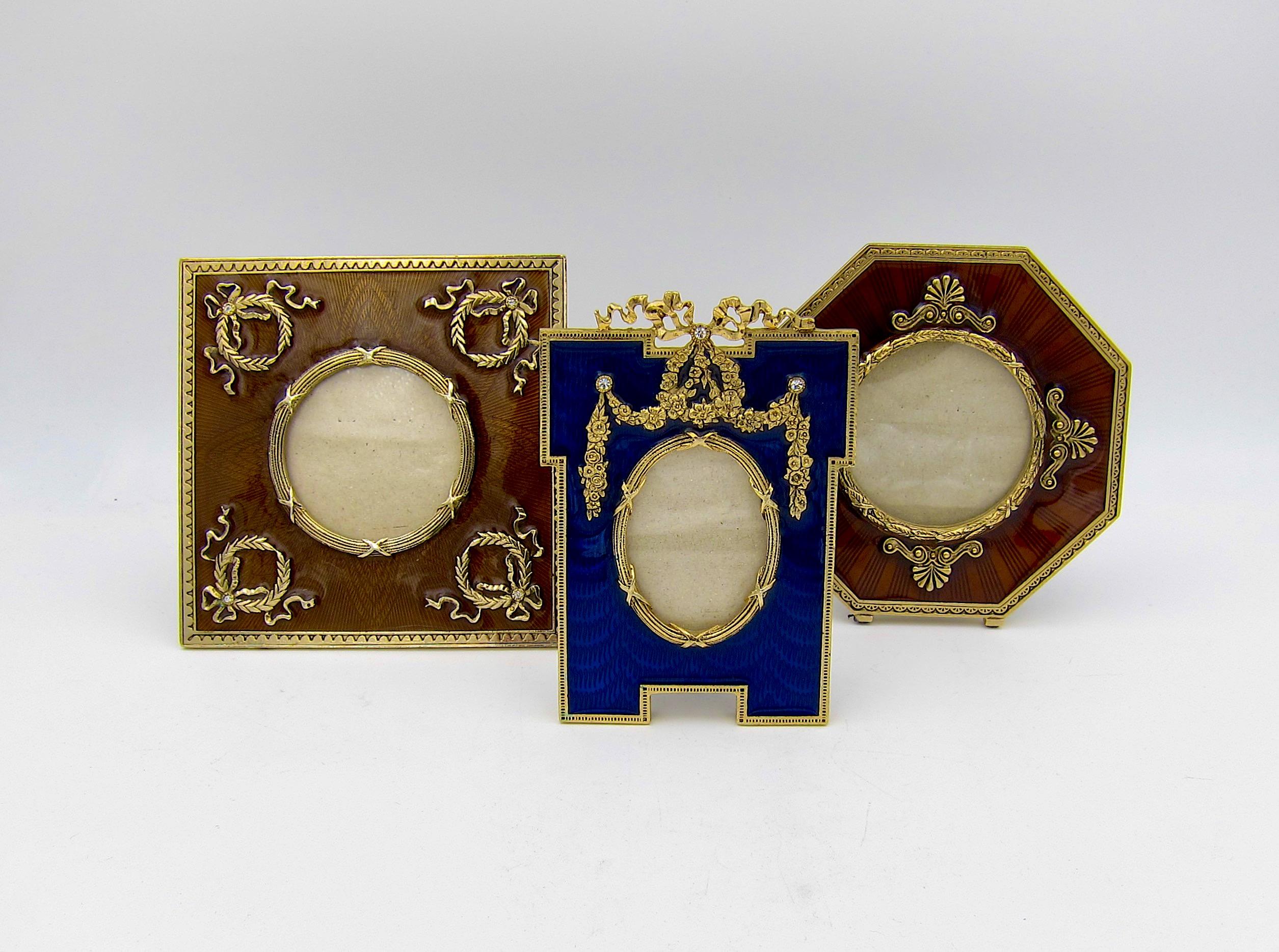 A vintage collection of three small ornamental picture frames decorated with jewel-toned enamel, neoclassical motifs, and faceted crystals. These tabletop photo frames of cast gold-colored metal are of substantial weight with easel backs and fields
