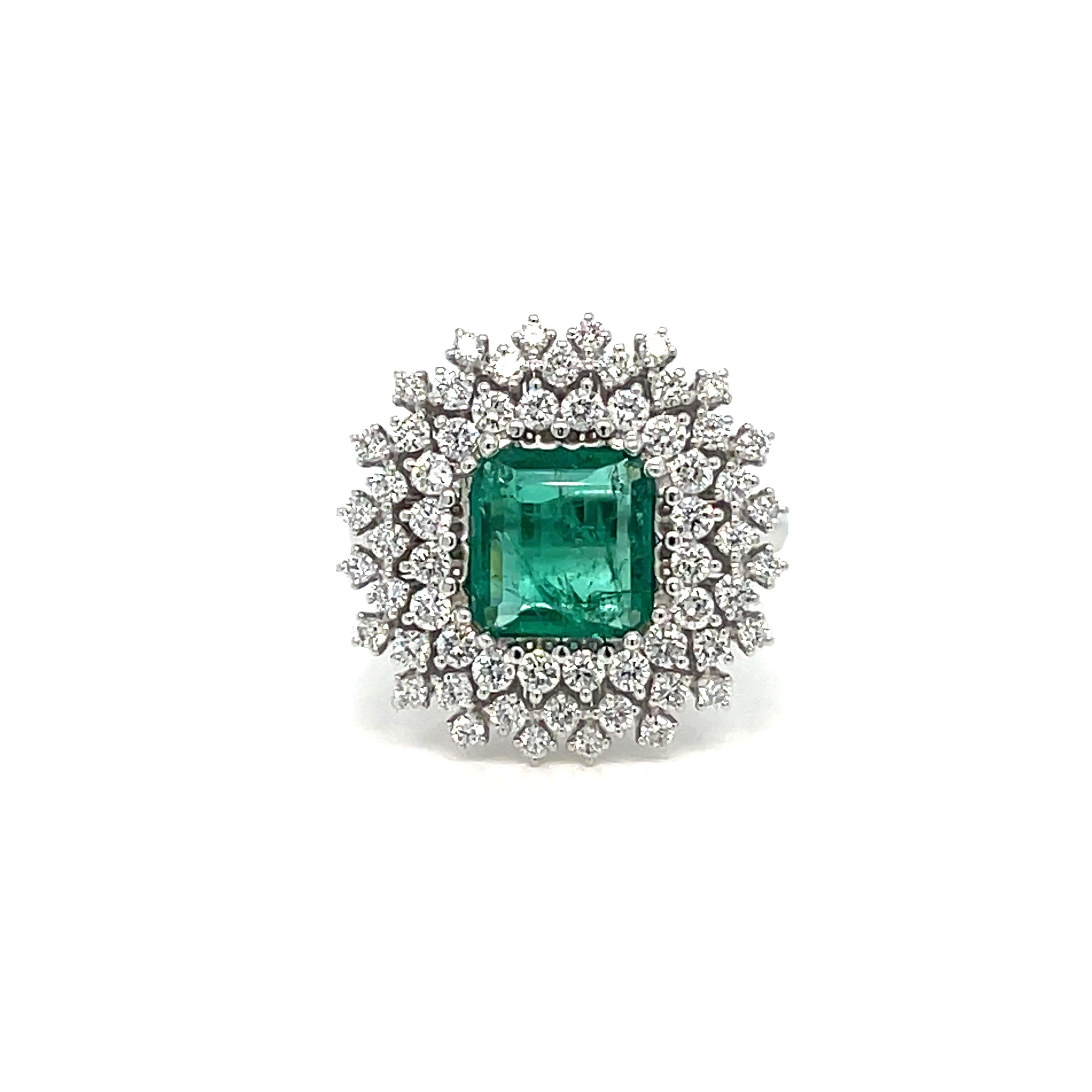 Beautiful cluster ring, hand-crafted in 18k white gold, centering a vivid emerald cut natural Emerald weighing 1.30 carat, Colombia origin, surrounded by 1.00 carat of round brilliant cut diamonds G color VVS. 
Origin Italy circa 1980

CONDITION: