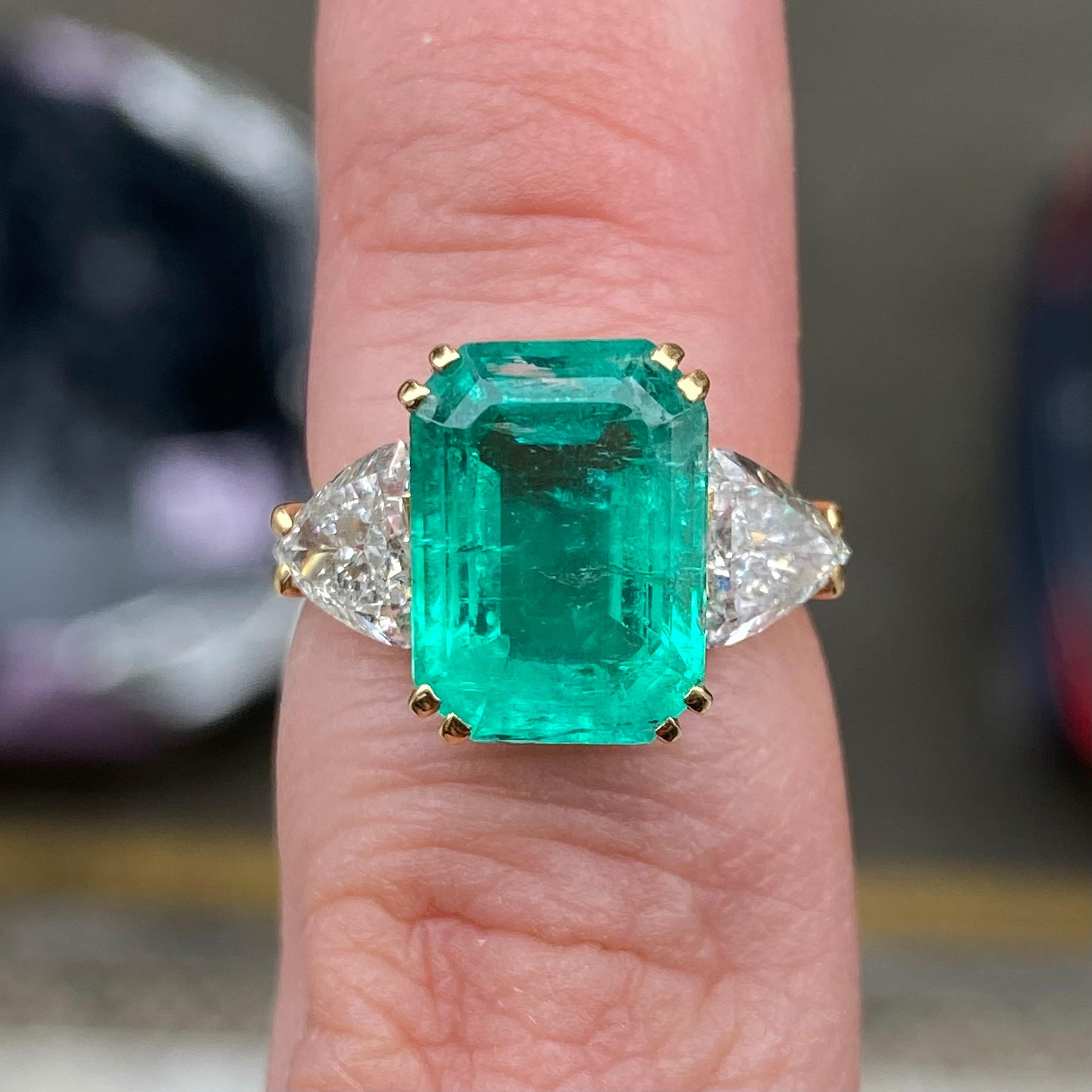Vintage certified 4.50-carat emerald and 1.40-carat trilliant-cut diamond three-stone engagement ring in 19.2 karat yellow gold, European, 1990s. This ring features a vibrant emerald-cut emerald (probably Colombian) double claw-set to the center,