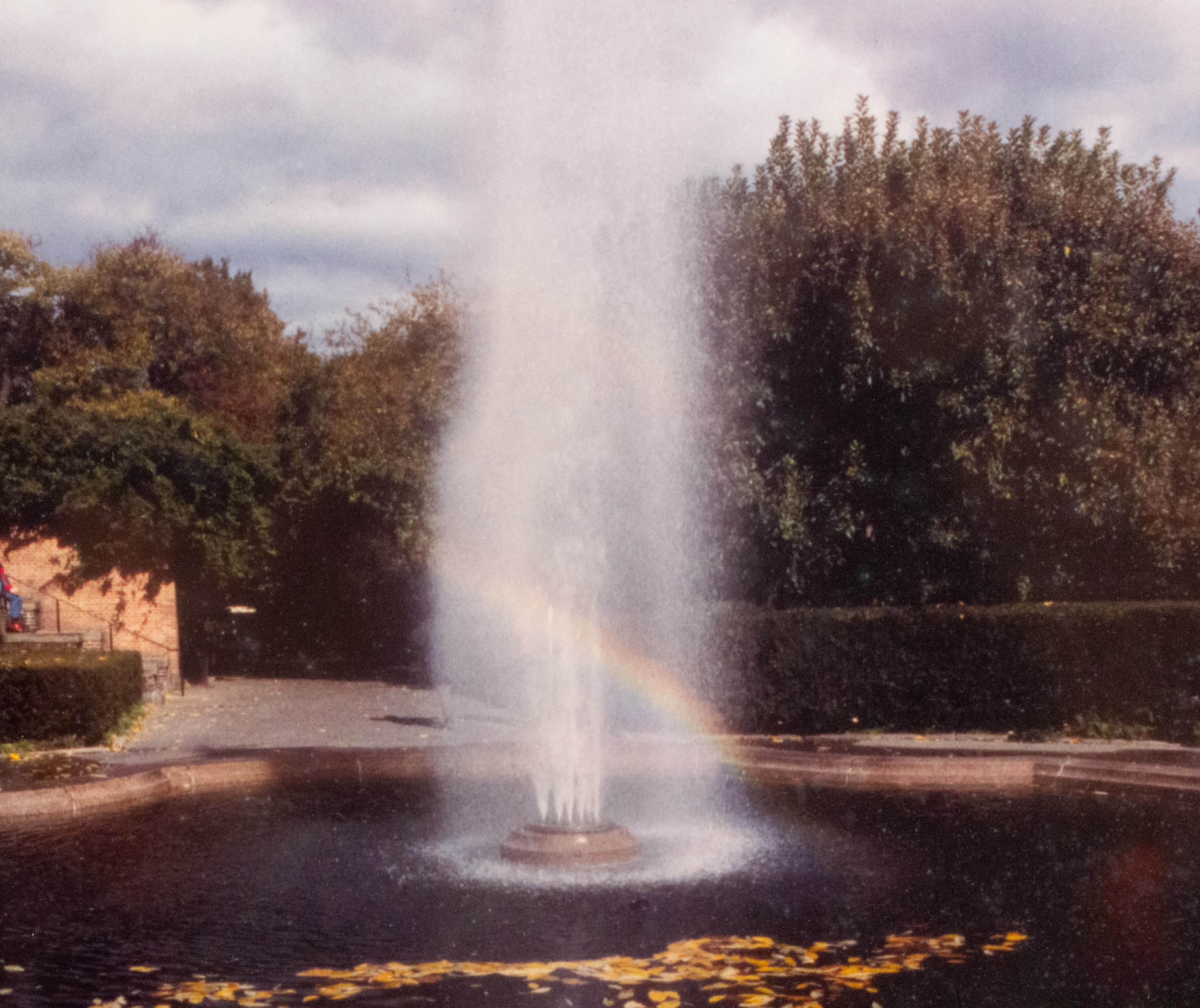 Vintage color photograph in a black frame of a fountain in a park with a rainbow. Photograph by Shelley Harrison.
     
