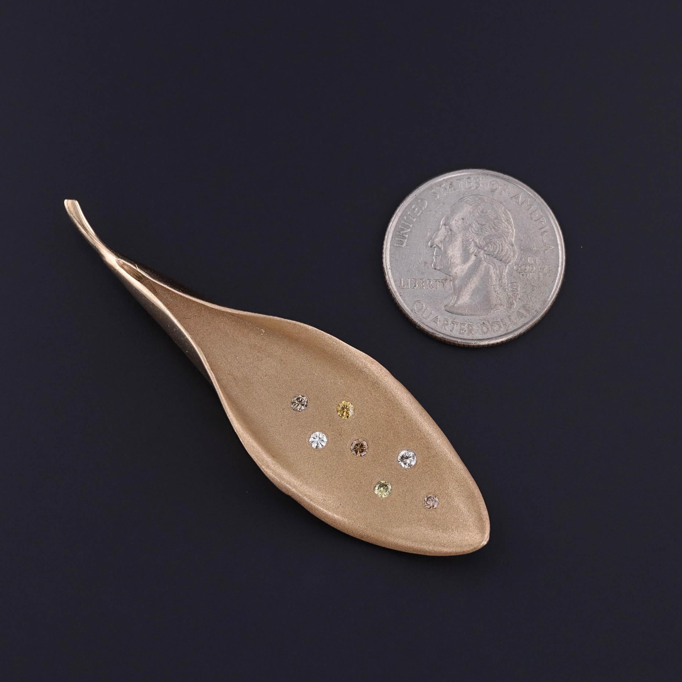 Vintage Leaf Pin: This 1990s brooch features a leaf of 14k gold, studded with colorful diamonds including yellow,champagne, and brown hues. The reverse is engraved with 'Love Always Mort 6-11-95'.

The piece measures 0.8 inches by 2.8 inches wide