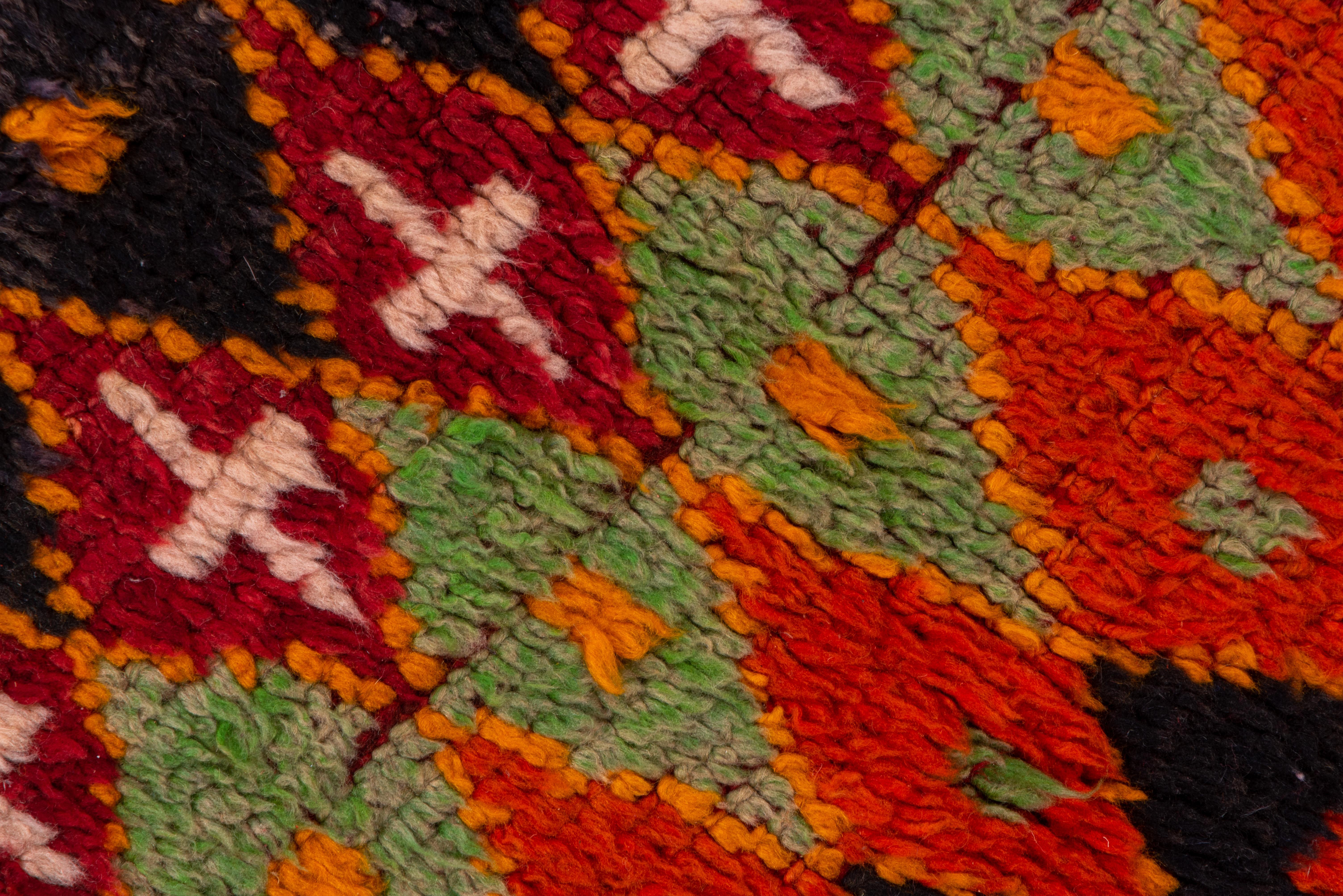 Rows and rows of small lozenges in red, yellow, orange, pale green, ecru, dark blue and rose constitute a close all-over border less mosaic pattern. At one end is a wide band of stripes in bold colors.