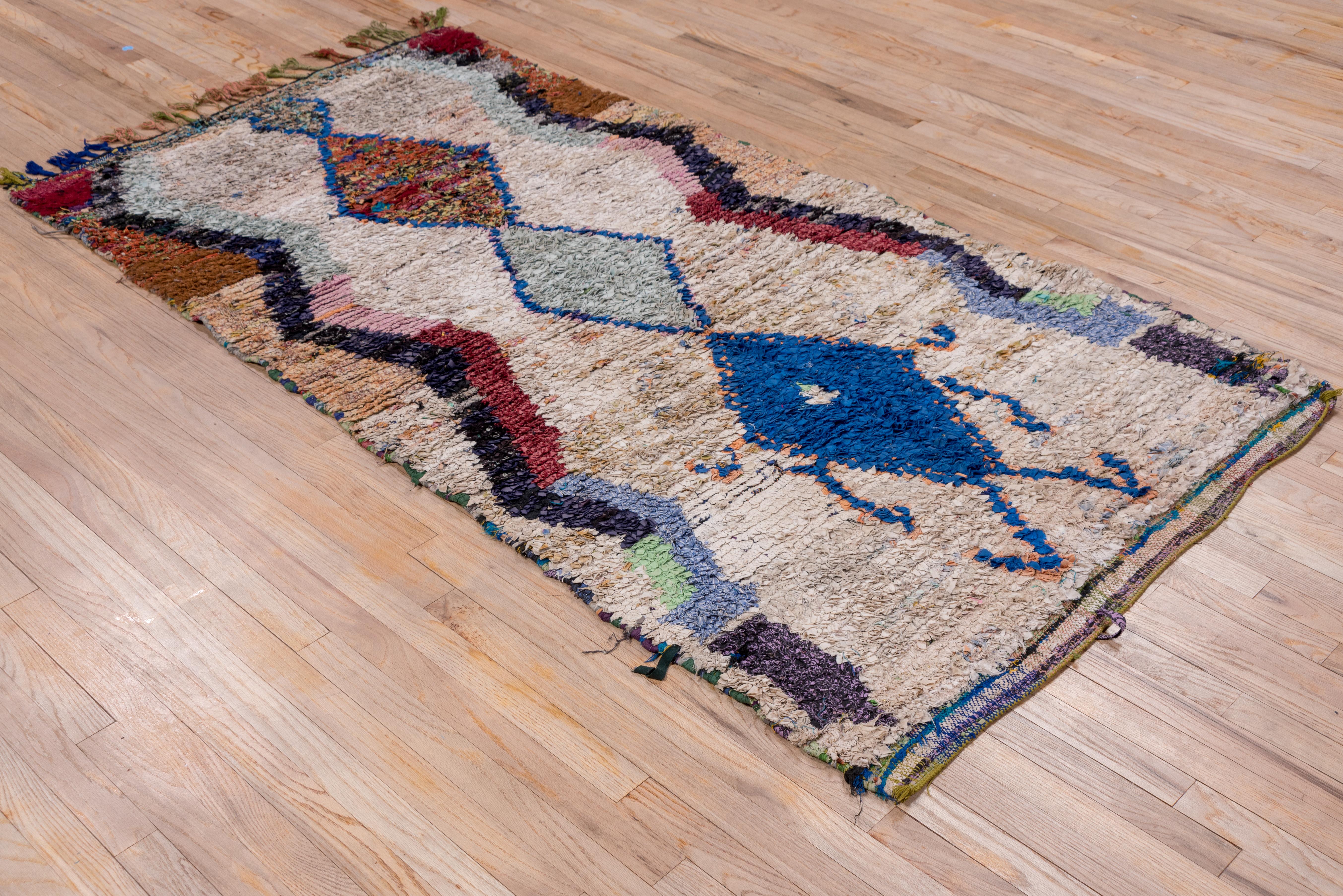 Instead of wool yarn, this modern tribal Moroccan scatter employs narrow strips of fabric in a simple lozenge panel pole medallion of speckled red, powder and blue, on a pearl ground. Lowest panel has arms and legs! Red and blue side zig-zags and