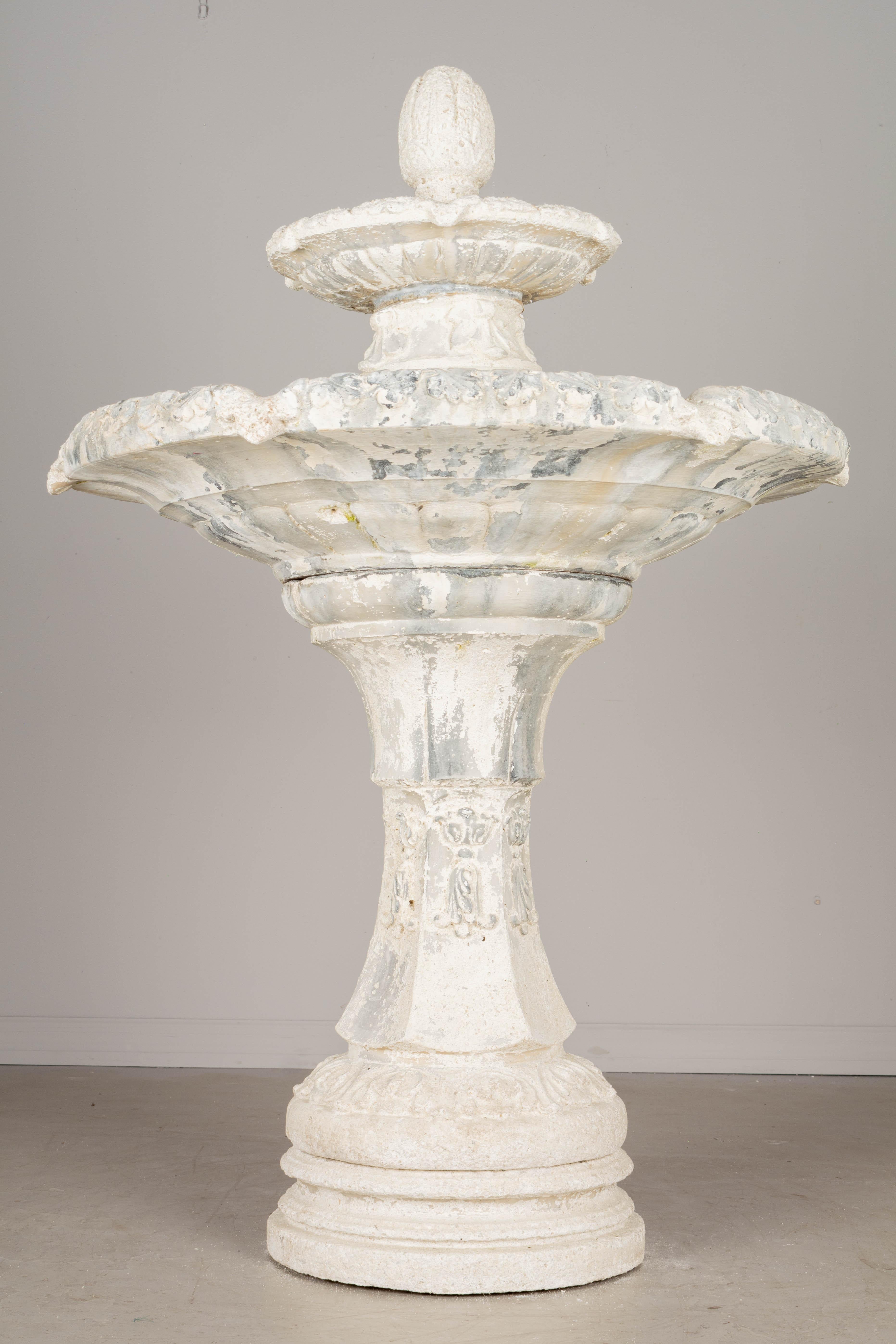 A vintage tiered garden fountain with pedestal base, two basins and a large finial. Decorative leaf pattern around the rim. Worn white patina. In six stacking parts. Made by Robinson Concrete Specialties. Circa 1980s. 
Dimensions: 62