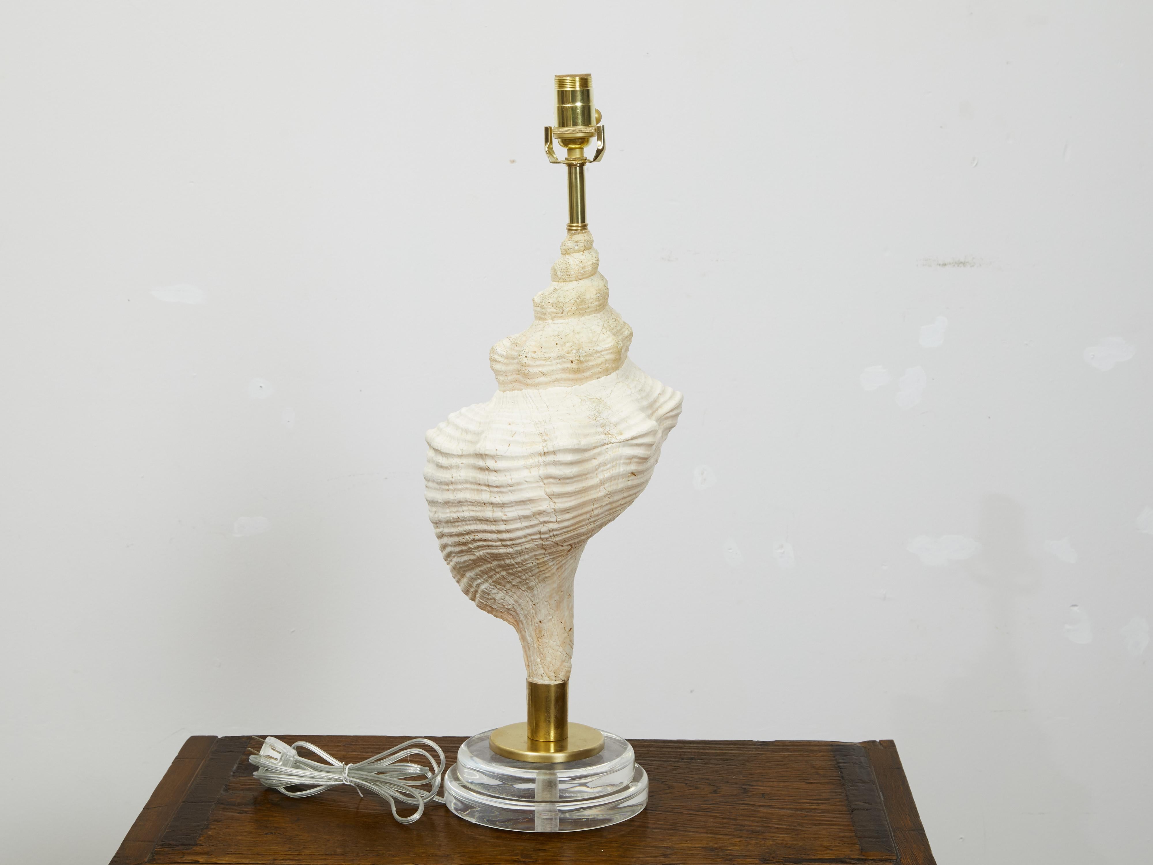 A vintage shell table lamp from the mid 20th century, mounted on round lucite base. Created during the midcentury period, this table lamp charms us with its elegant conch shell mounted on brass and raised on a circular stepped lucite base. Wired for
