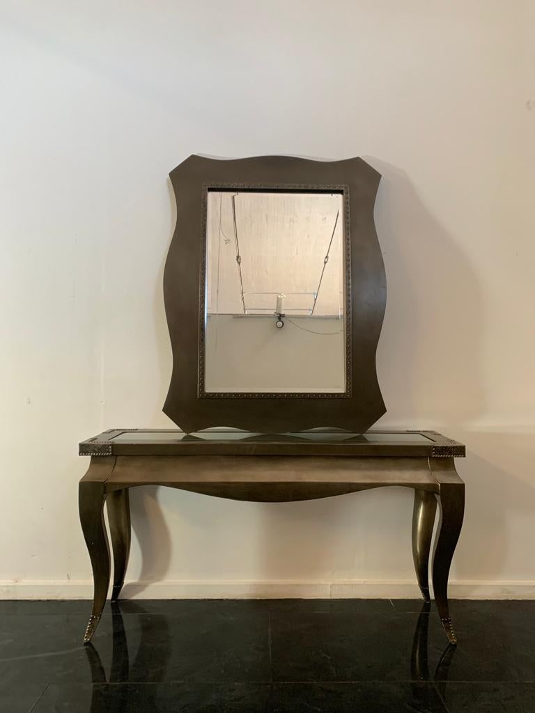 Conjunto ecléctico compuesto por consola y espejo, años 80. Acabado metálico bronce, esquinas y puntas metálicas. La consola mide 77 cm de alto, 147 cm de ancho y 40 cm de fondo. El espejo mide 130 cm de alto, 97 cm de ancho y 7 cm de